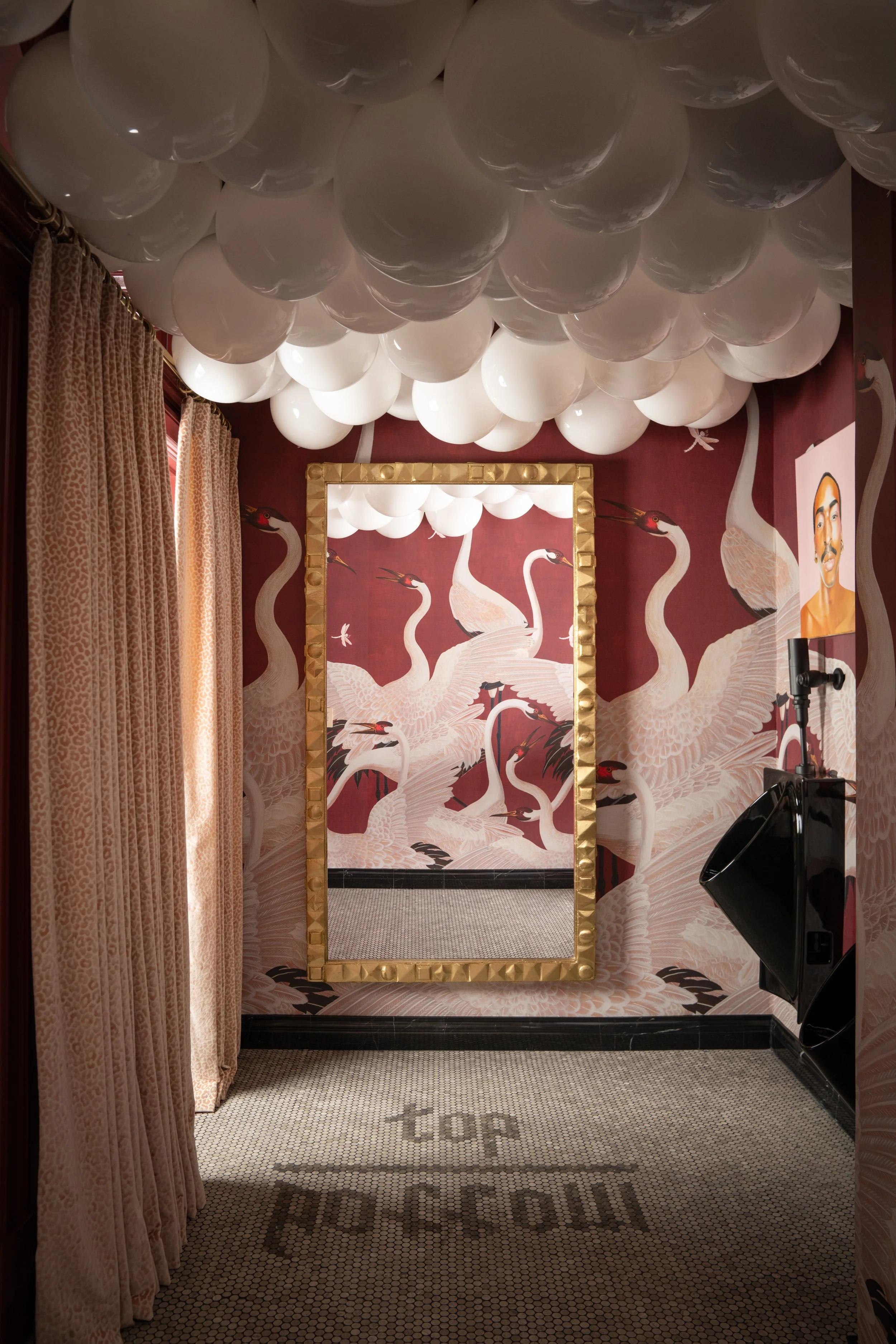 A photo taken inside a room with red walls decorated with white crane illustrations, a large gold-framed mirror, white balloons attached to the ceiling, a portrait of a man on the wall, and a black hair dryer station on the right. Captured by Jeff Jo