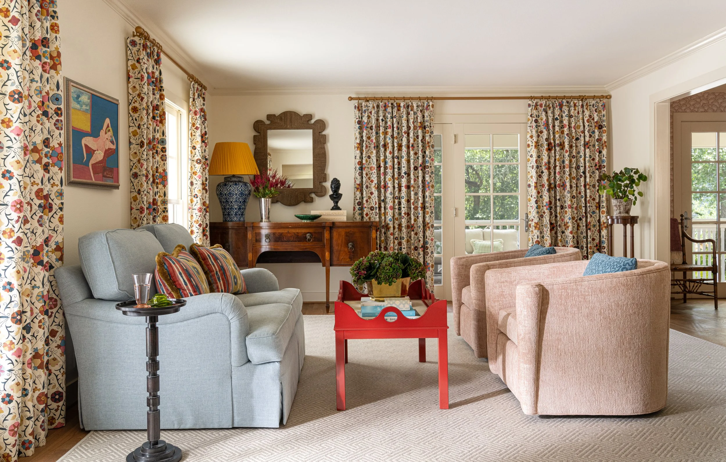 Interior design photography by Texas-based photographer Jeff Jones. Vibrant living room with floral curtains, pastel furniture, red coffee table, and eclectic decor, full of natural light.