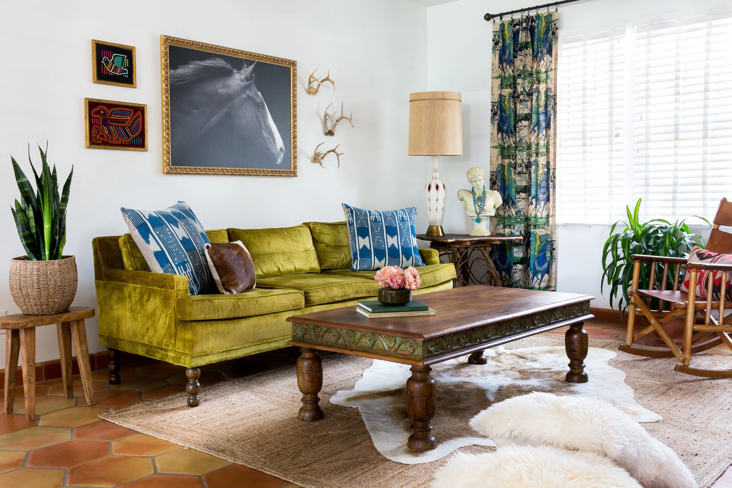 Interior design photography by Jeff Jones showcasing a Spanish-inspired living room in Austin, Texas, featuring a green velvet couch, clay tile floors, white walls, and a warm Southwest vibe.