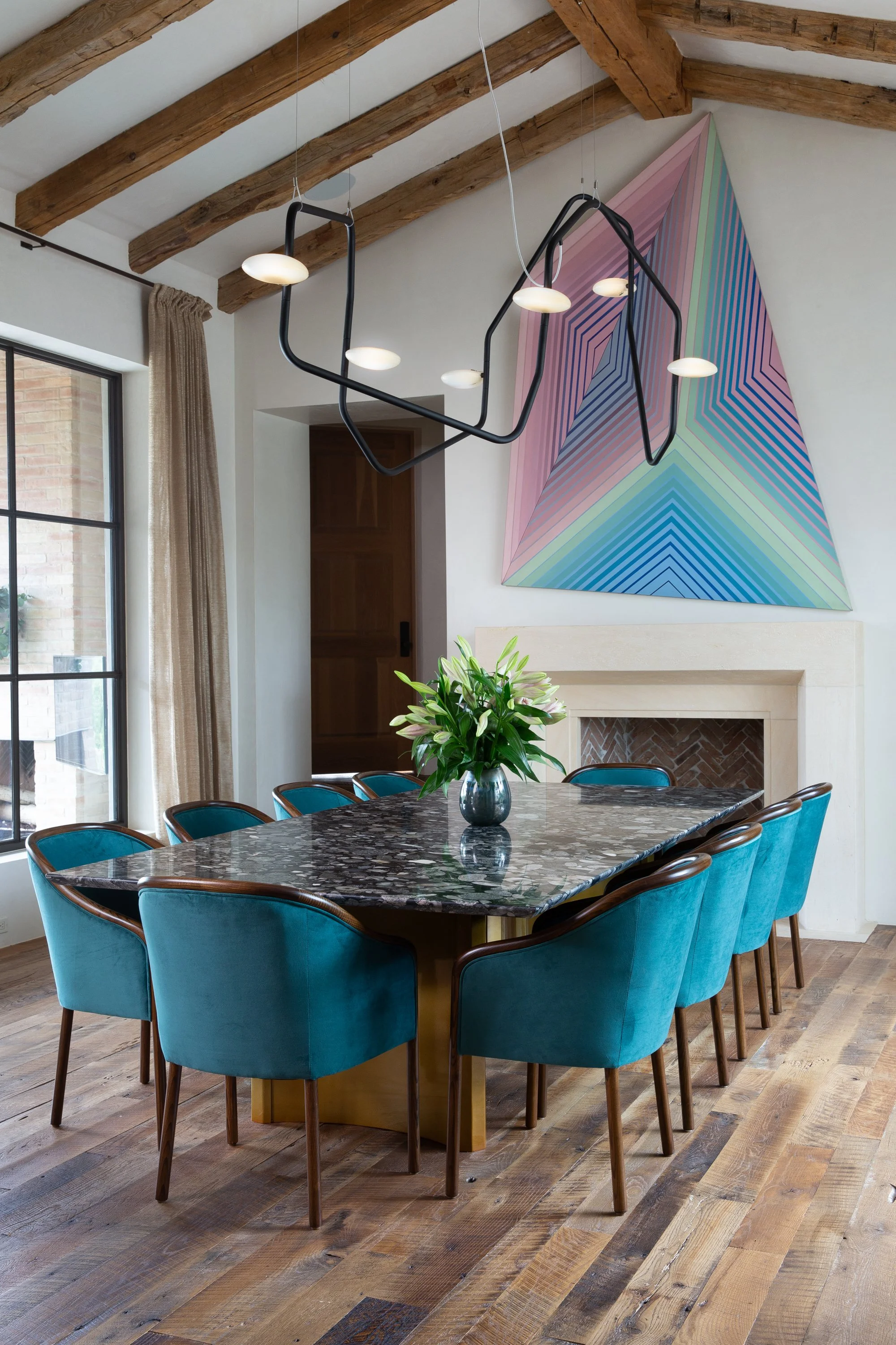 Interior design photography by Jeff Jones featuring vaulted ceilings with beams, modern light fixture, custom artwork over fireplace, and teal dining chairs in a stylish Austin, Texas home.