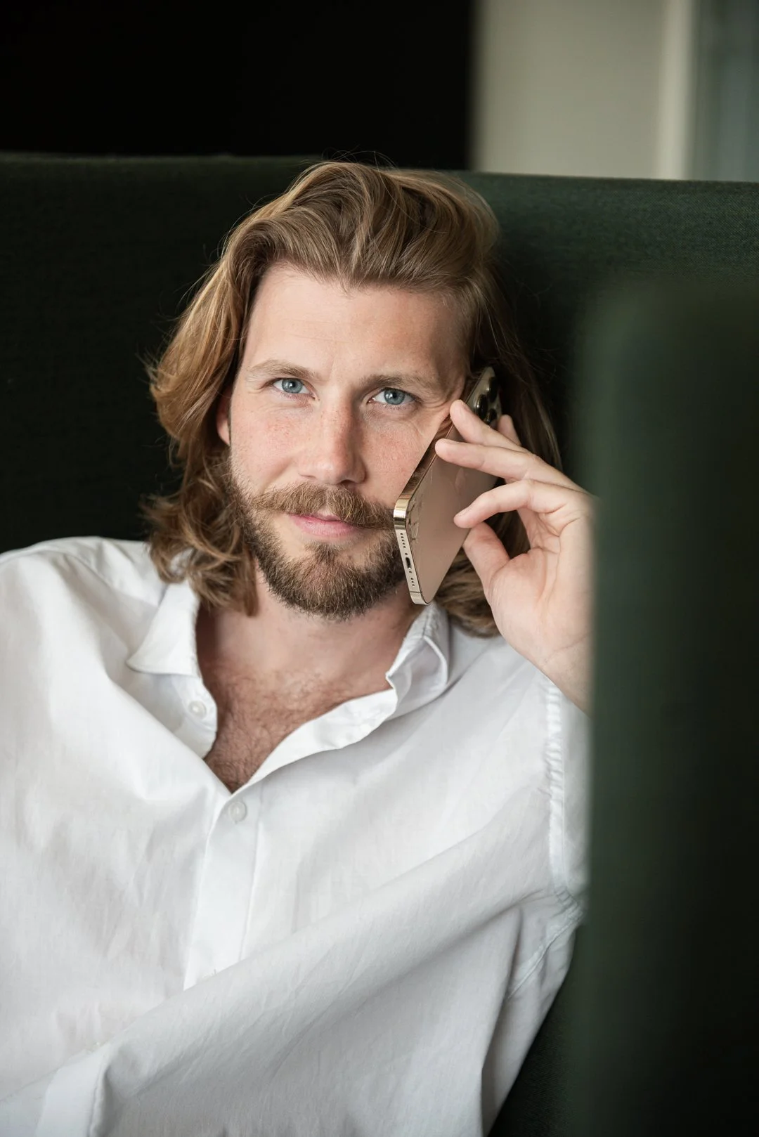 Man med långt, ljusbrunt hår och skägg, sitter i en soffa och pratar i mobiltelefon.