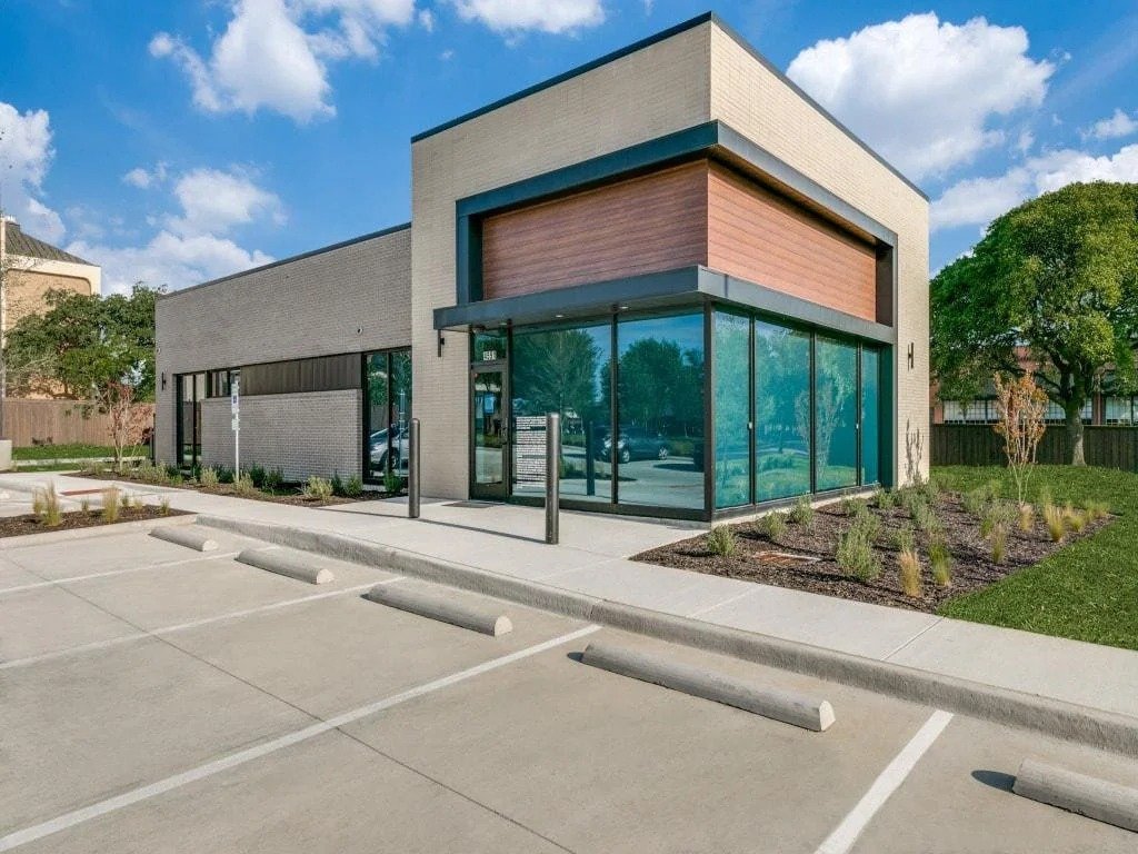 Modern commercial building with large glass windows and a landscaped parking lot.