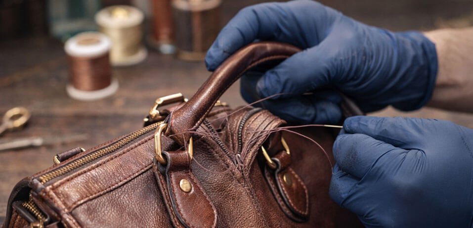 Specialist reinforcing damaged handles on a luxury leather handbag using professional stitching techniques