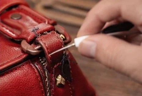 Poor DIY repair on a luxury handbag handle showing uneven stitching and damage