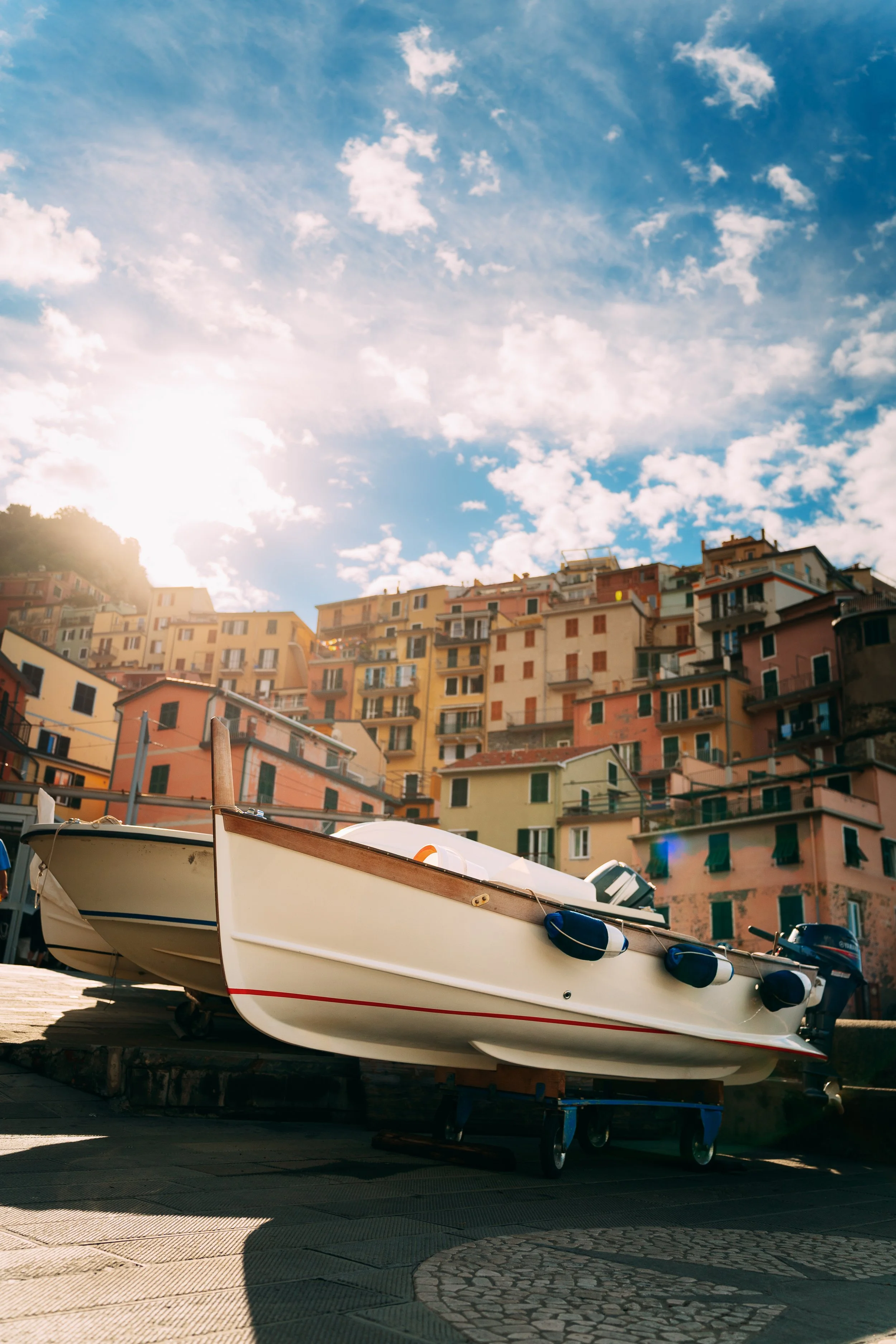 Boats on a paved dock in front of colorful hillside buildings under partly cloudy sky.