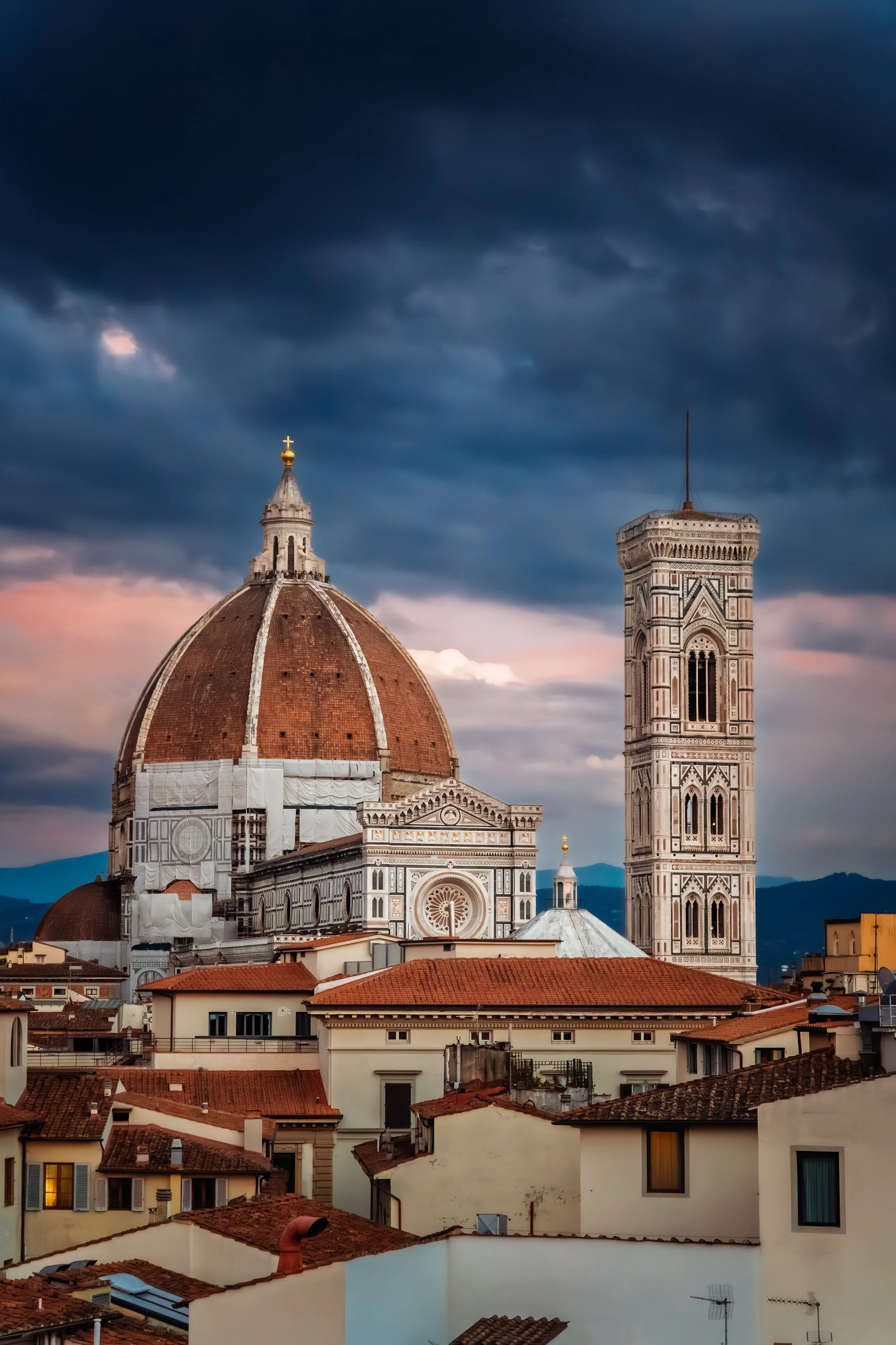 The image shows the Florence Cathedral with its large dome and the adjacent bell tower, set against a dramatic, dark cloudy sky at dusk.