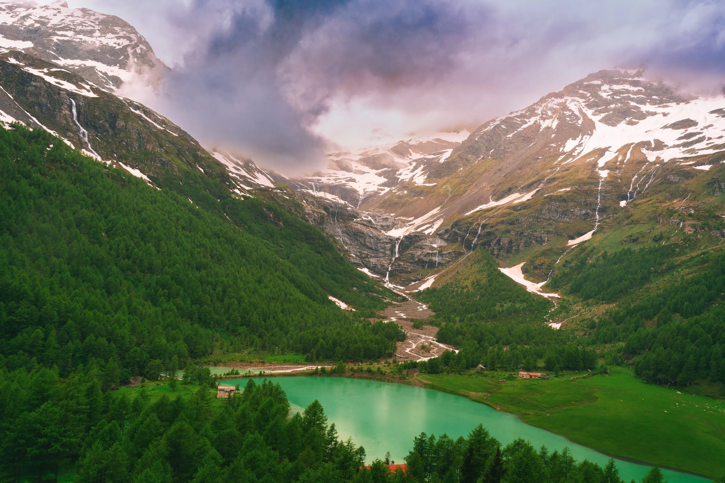 Snow-capped mountains with a green forest and turquoise lake.
