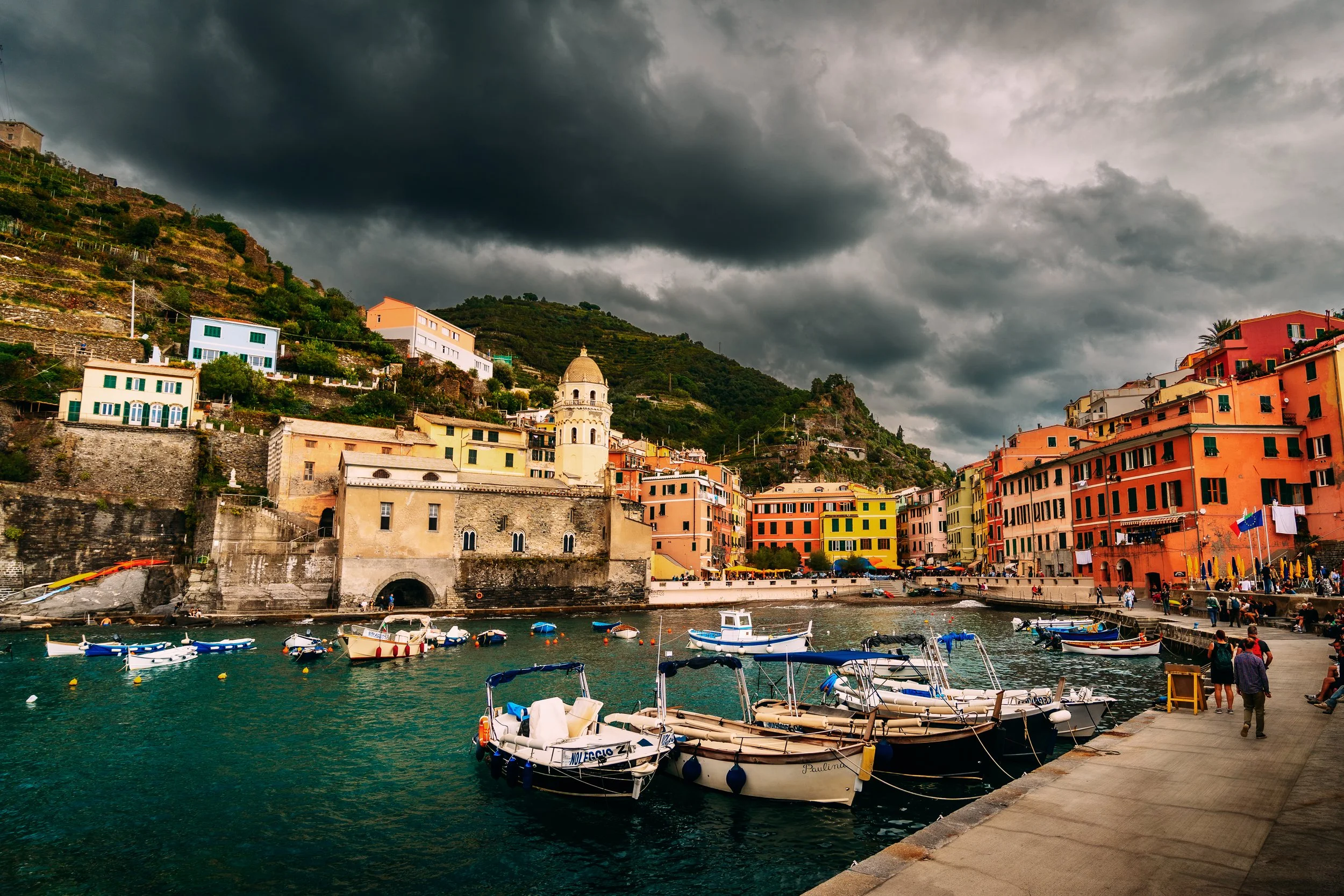 Colorful buildings and boats docked at a harbor on a cloudy day in a Mediterranean coastal town.