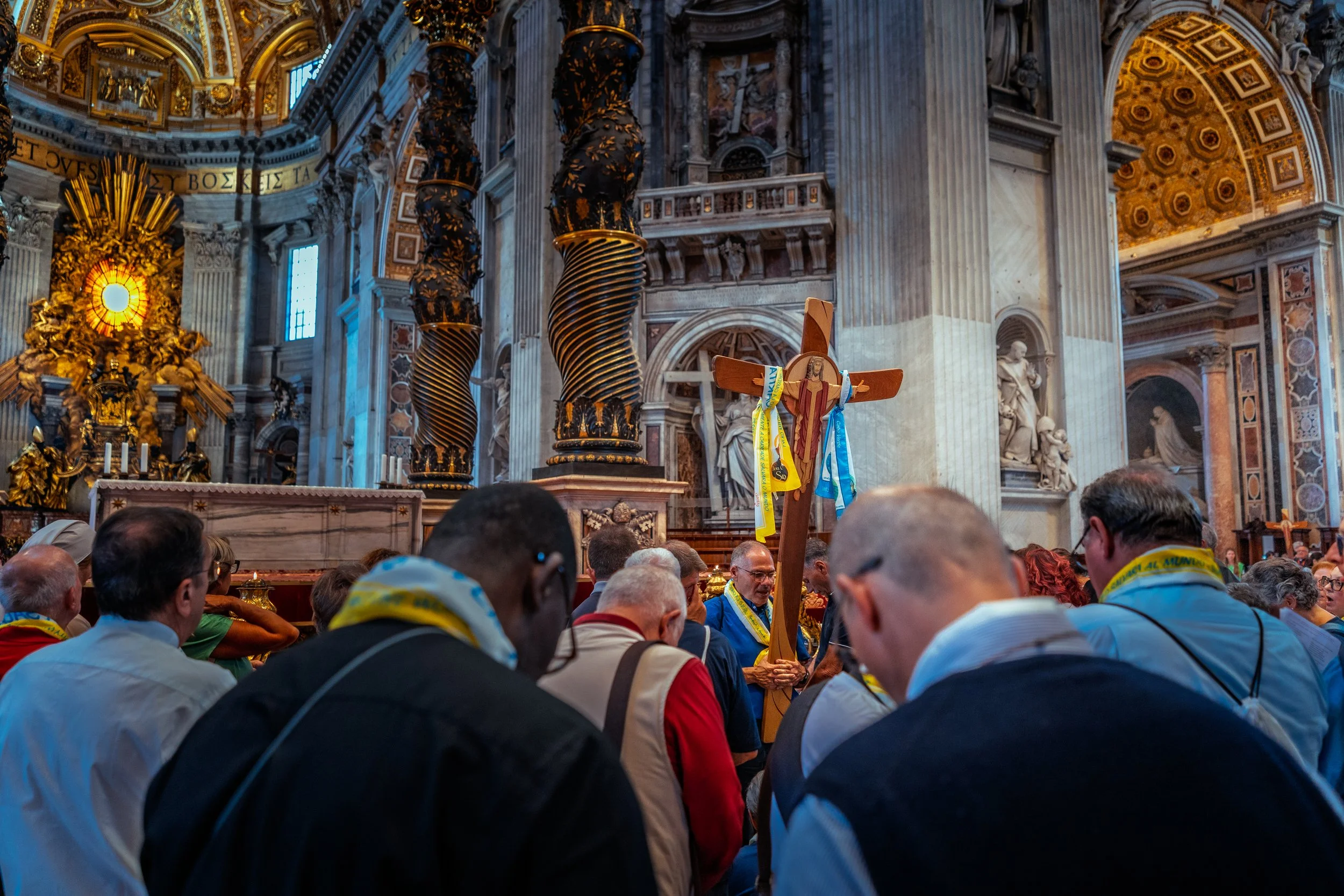 People gathered inside a cathedral holding a cross with religious iconography, during a religious ceremony or procession.