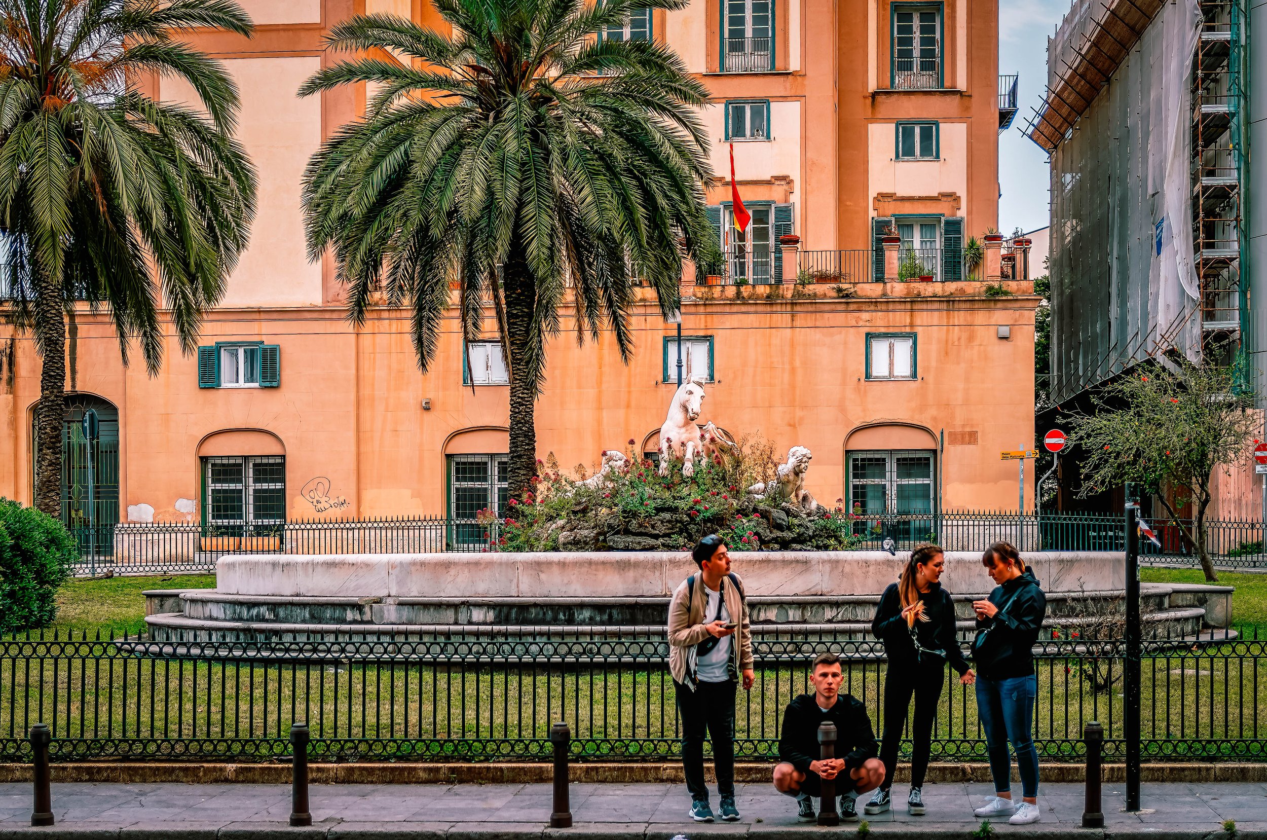 Group of people in front of a building with palm trees and a fountain