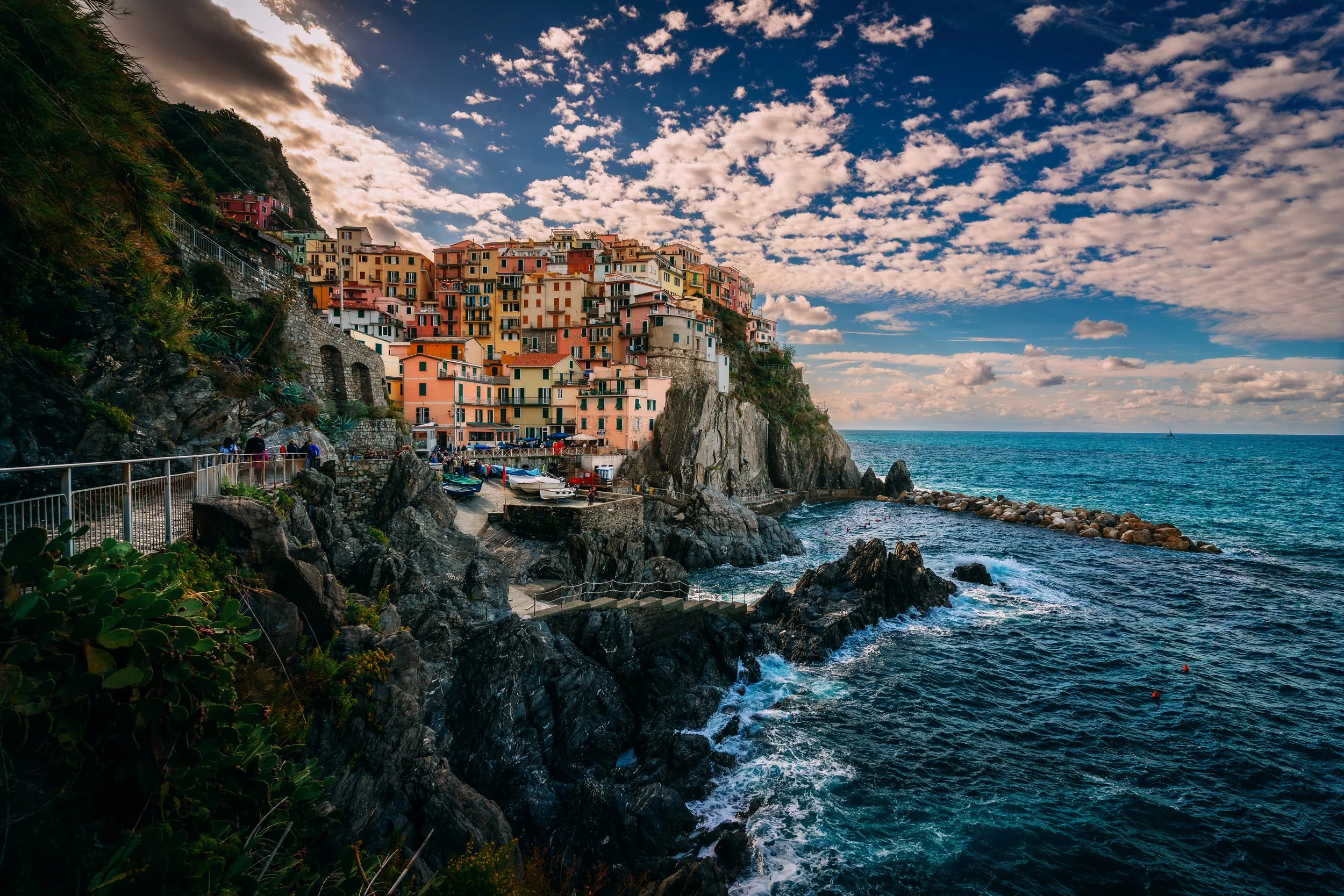 Harbor scene in Capri, Italy, with colorful buildings and boats, including Blue Grotto tour boats, against a hillside backdrop.