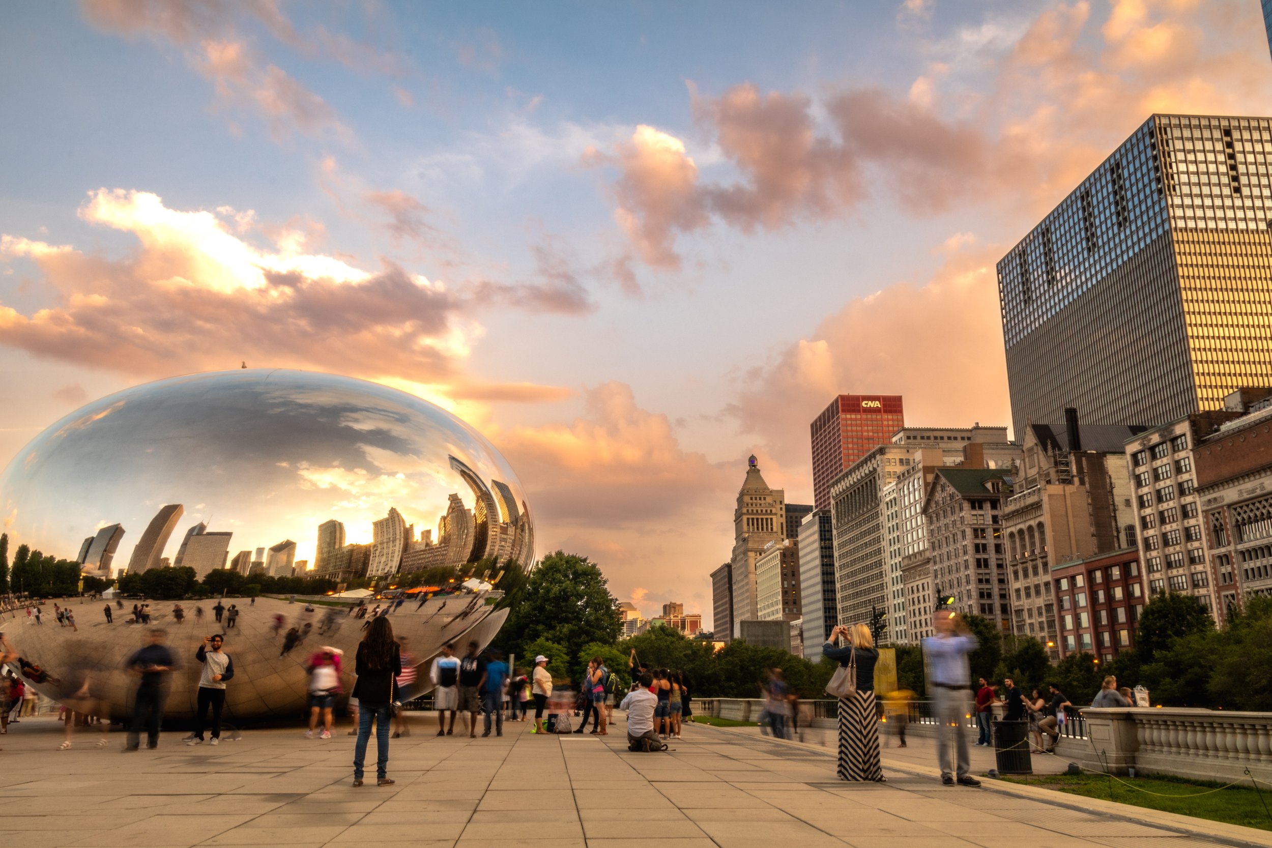 Cloud Gate sculpture in Chicago's Millennium Park with people walking and city skyline at sunset