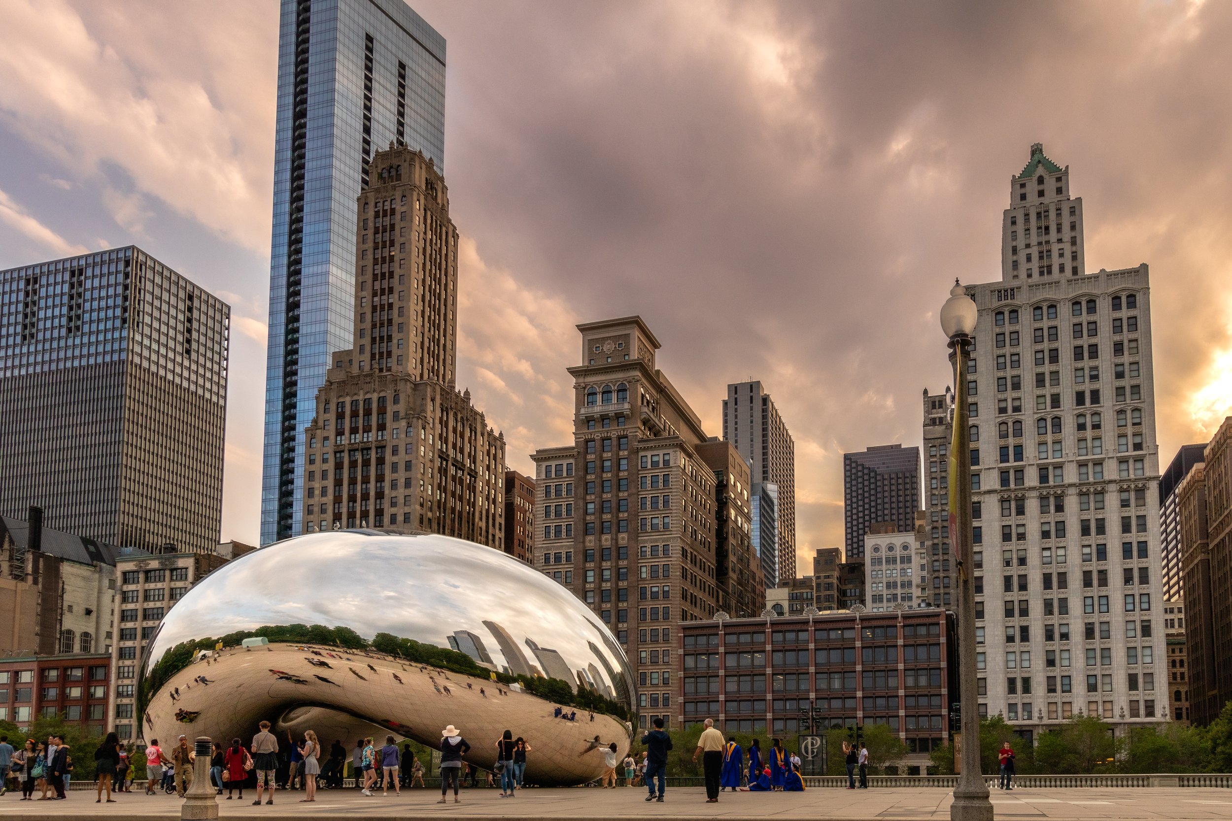 The Cloud Gate sculpture, also known as "The Bean," in Millennium Park, Chicago, surrounded by people and city buildings.