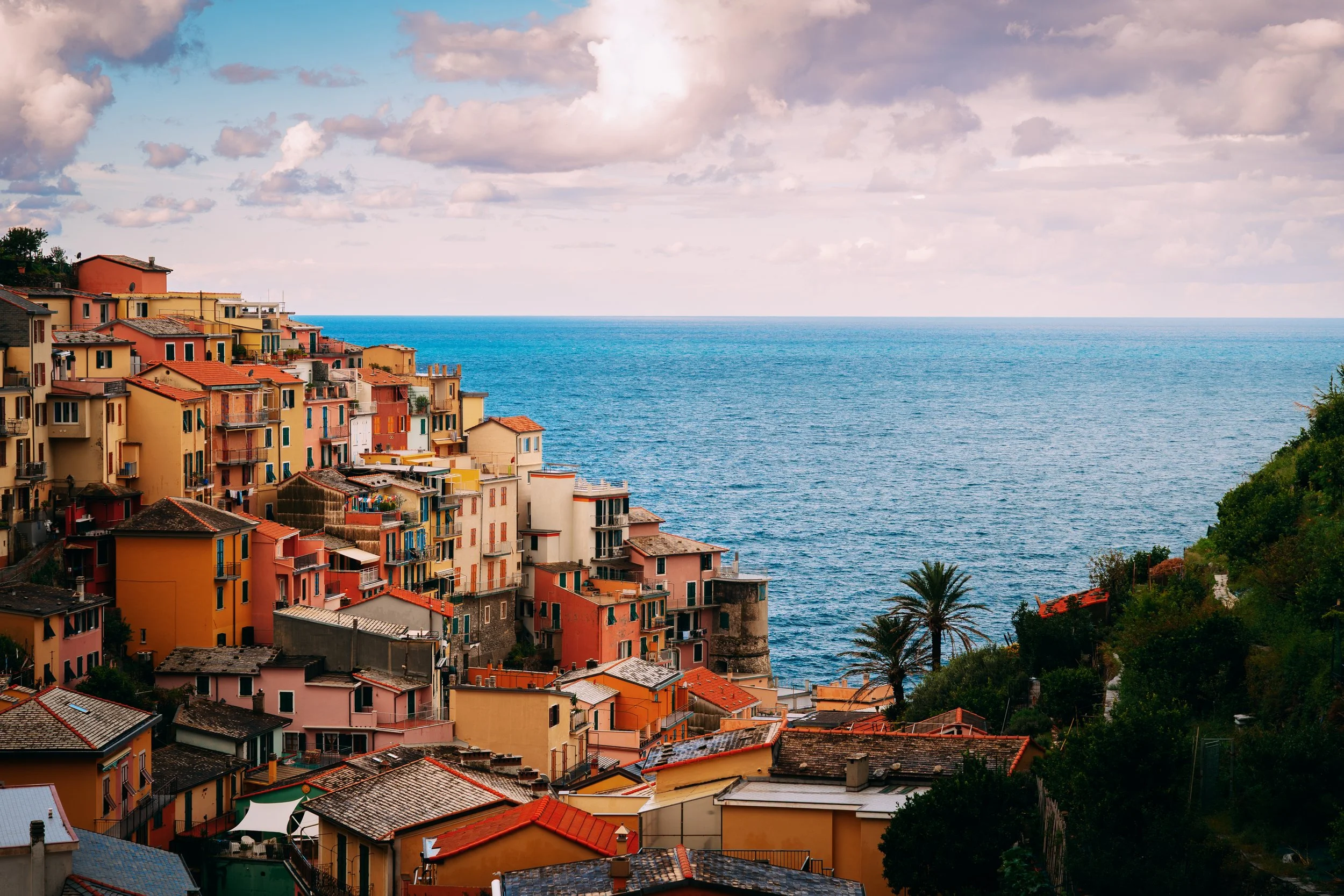 Colorful hillside buildings overlooking the sea with a cloudy sky overhead.