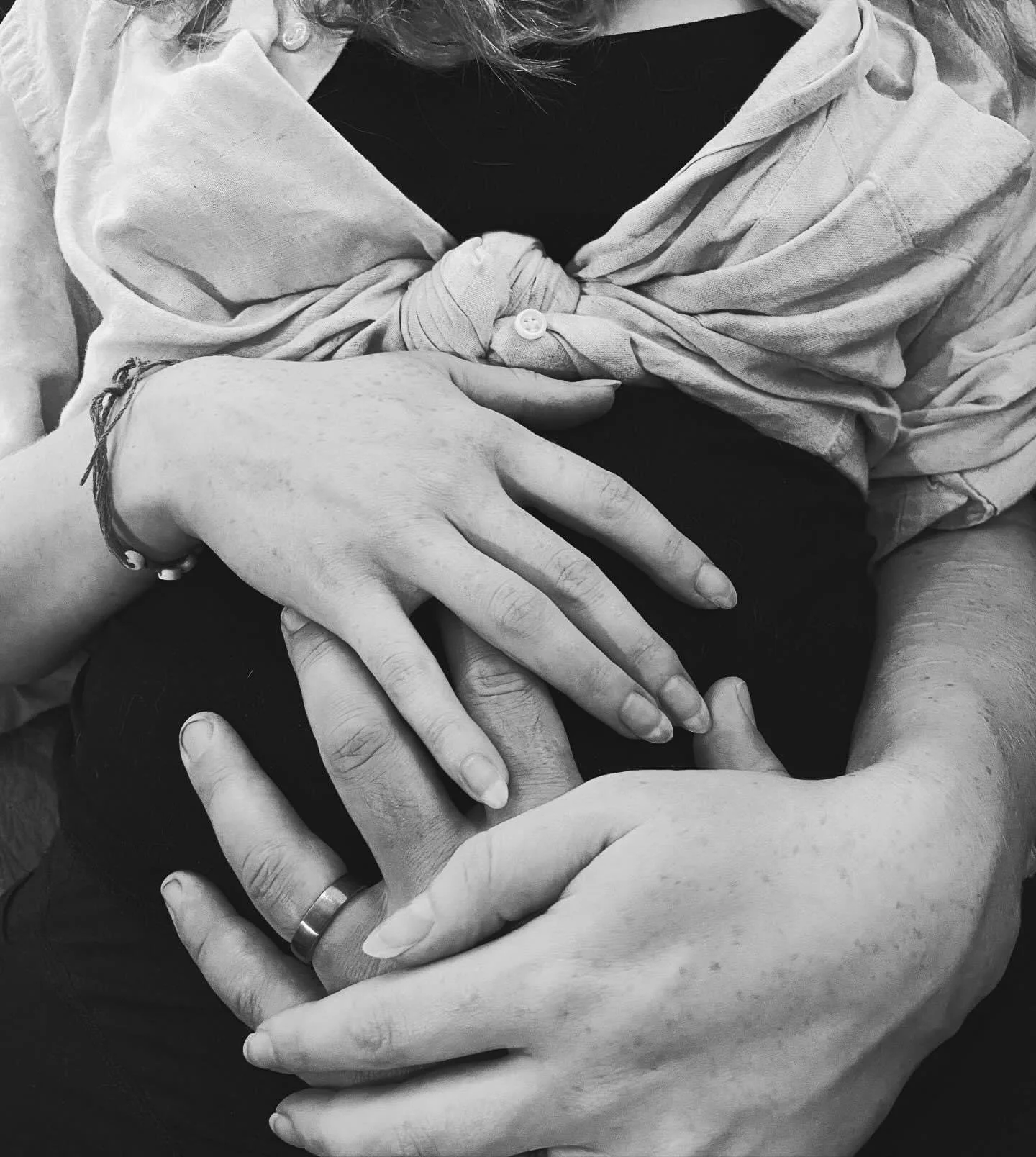 A black and white image of a mother and father's hands laid over a pregnant belly
