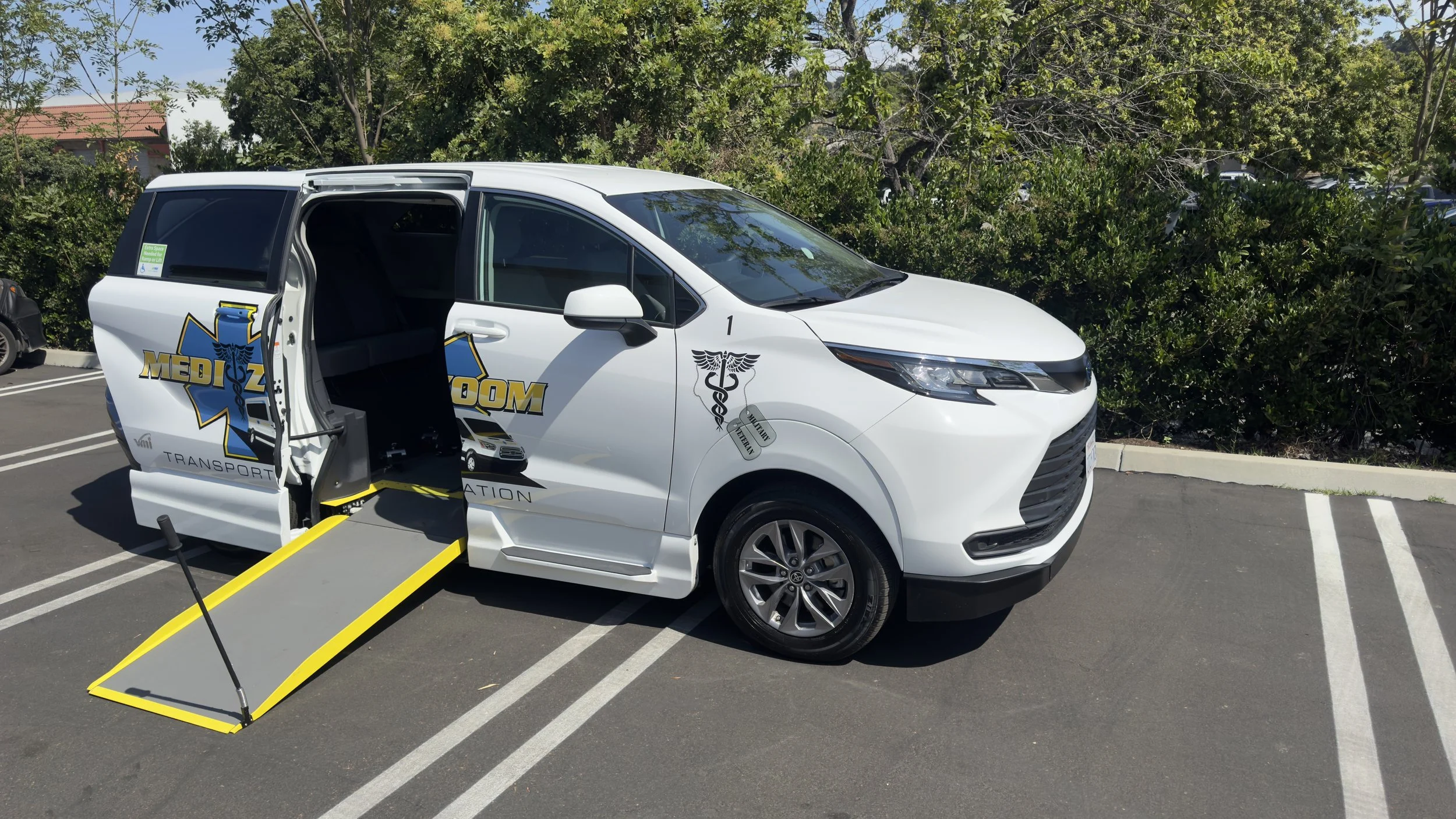 A white transport van with medical symbols and the words 'Medical Transportation' written on the side, parked in a parking lot with a wheelchair ramp extended from the side door.