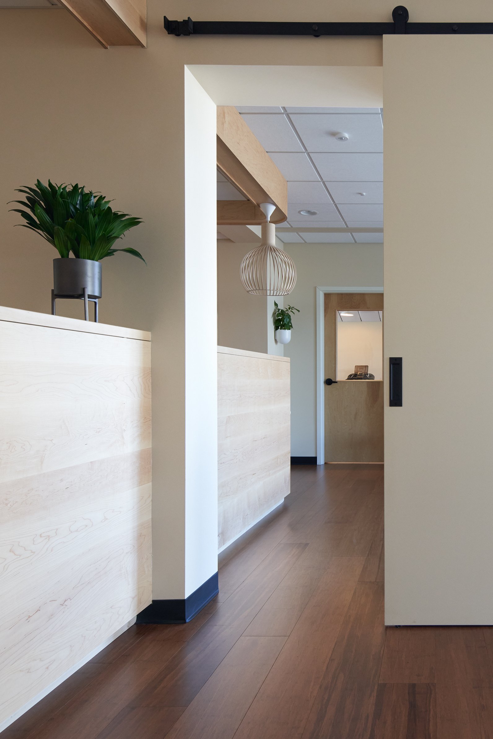 Modern interior space with wooden floors, light-colored walls, decorative plants, and hanging light fixtures.