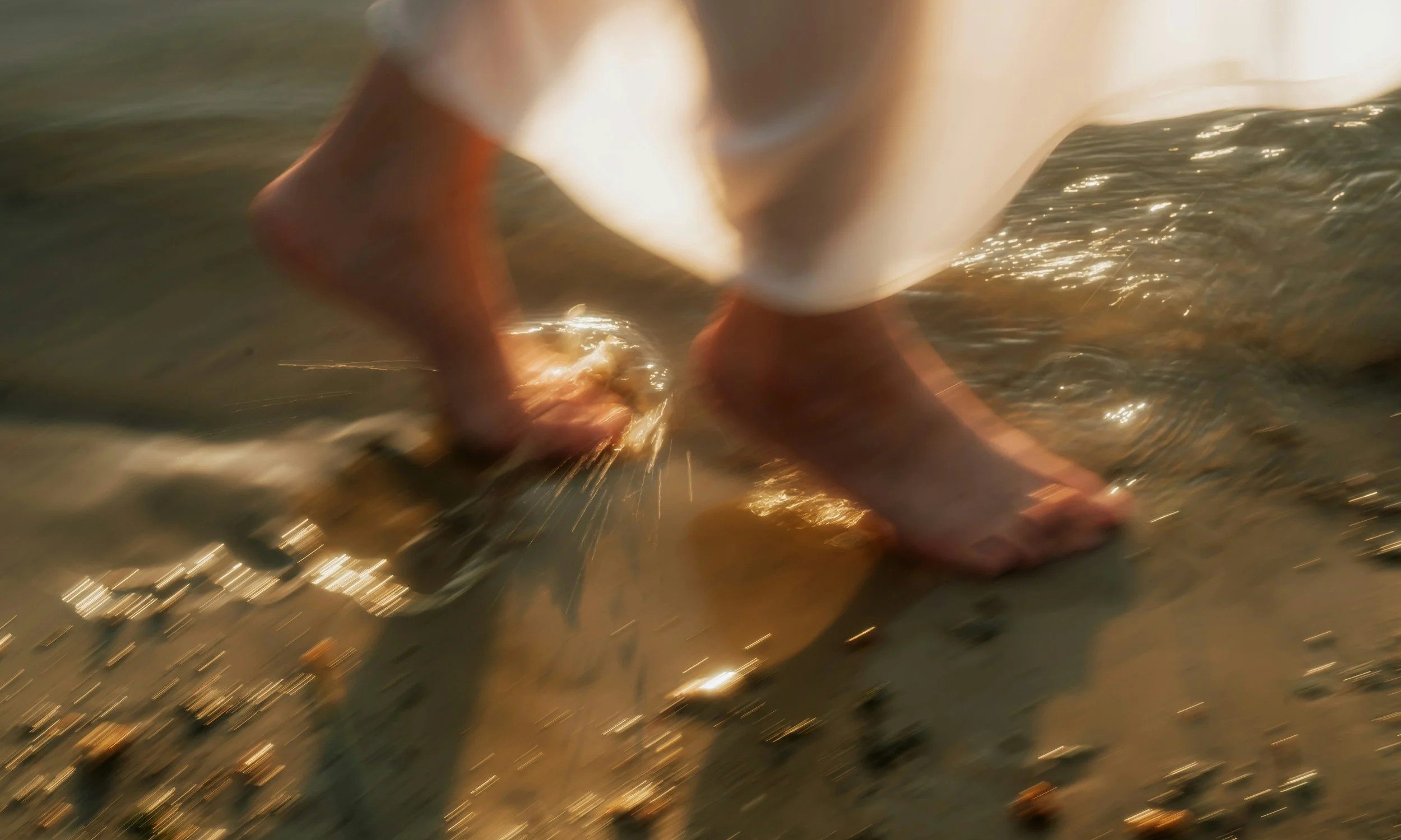 Bare feet walking through sunlit shallow water on the shore, symbolizing the start of a new journey