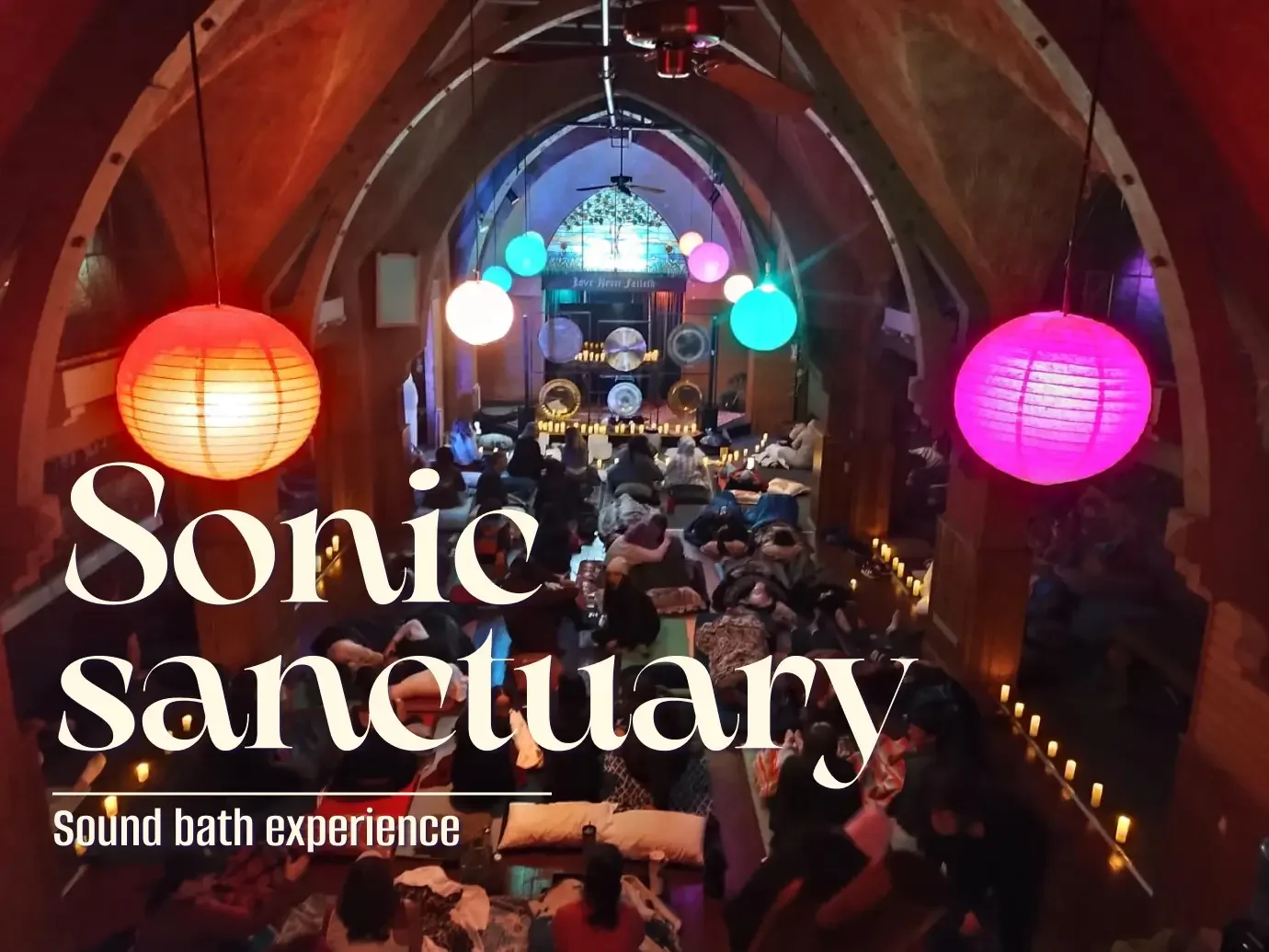 People attending a sound bath experience at Sonic Sanctuary with colorful hanging lanterns and candles in a wooden arched ceiling room.