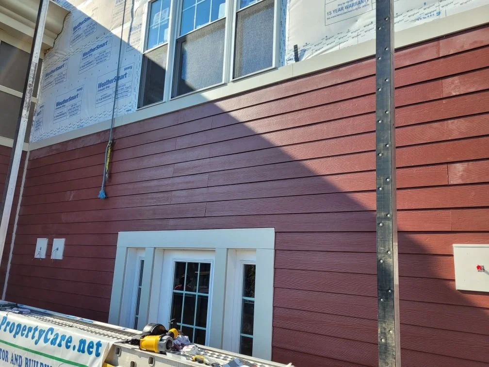 Exterior of a house under construction with red siding, a window, and scaffolding.
