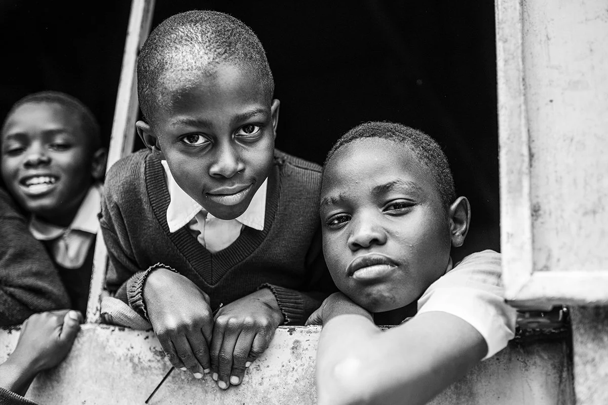 Three young boys looking through a window with serious and happy expressions in black and white.