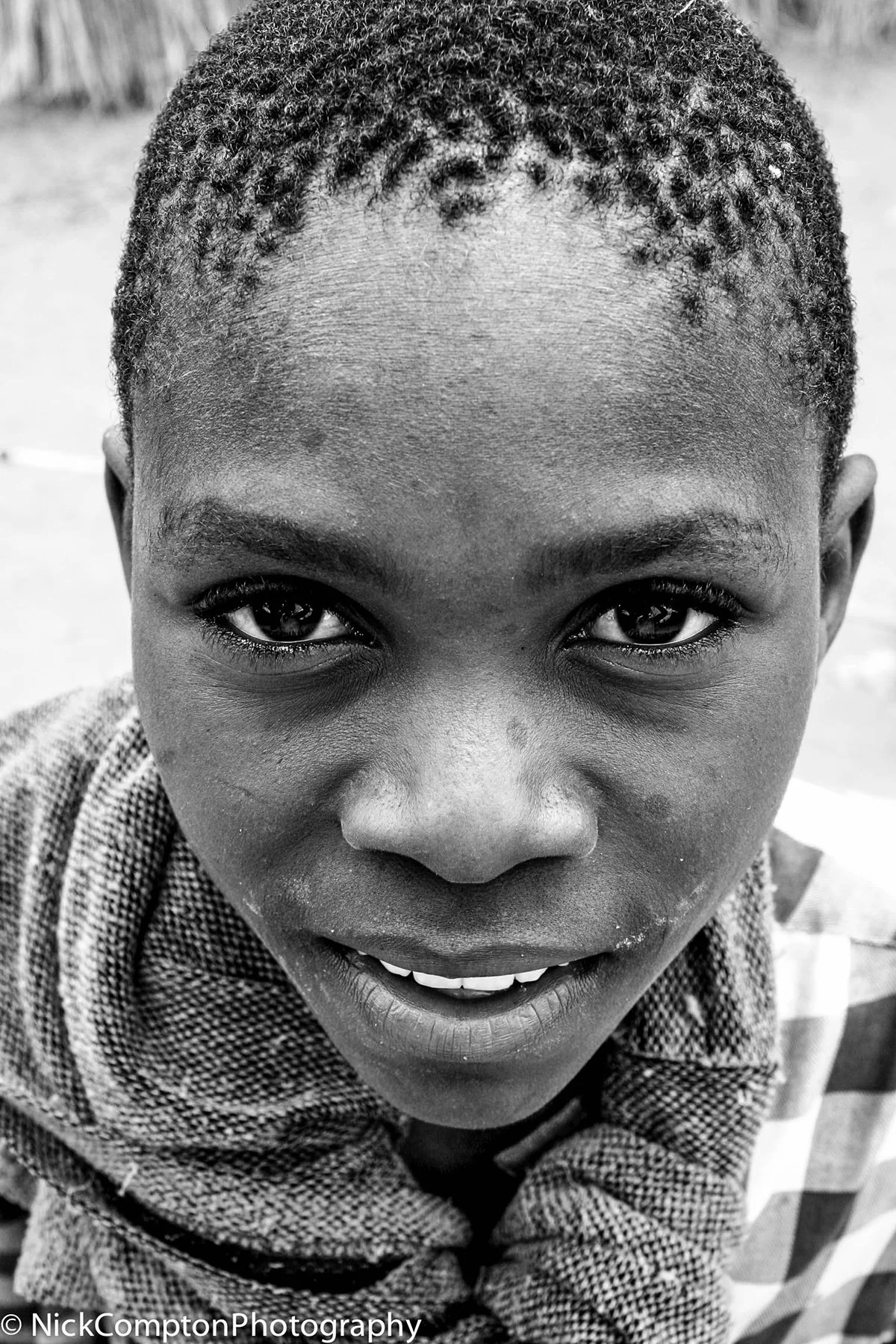 Close-up black and white portrait of a young boy smiling outdoors, with curly hair and expressive eyes.
