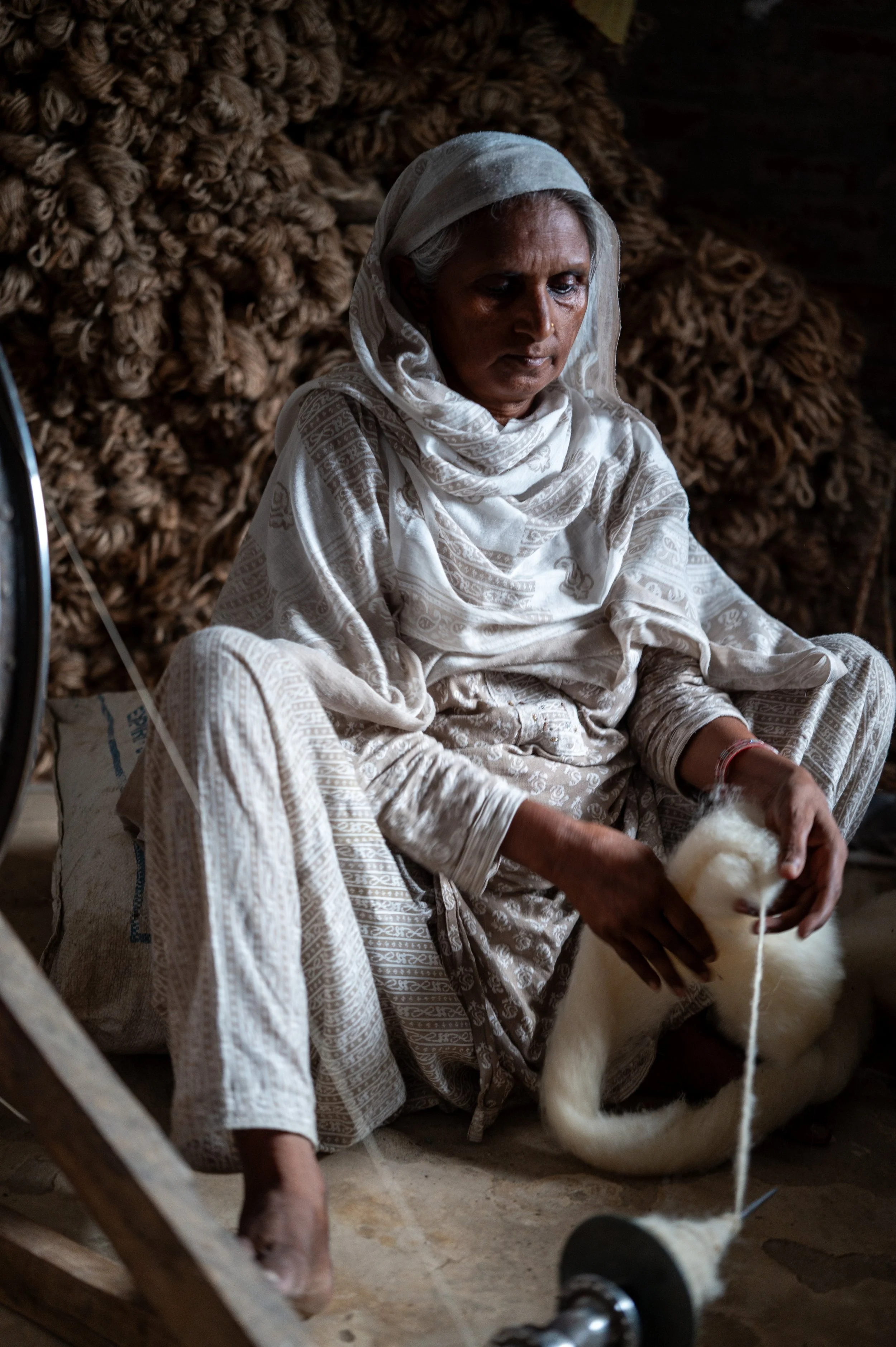 THE KEEPER OF THREADS
A masterclass in the "Narrative of Resilience." This portrait captures the focused intensity of the spinner. The play of light across her weathered hands and the rhythmic motion of the wheel represent the foundational strength o
