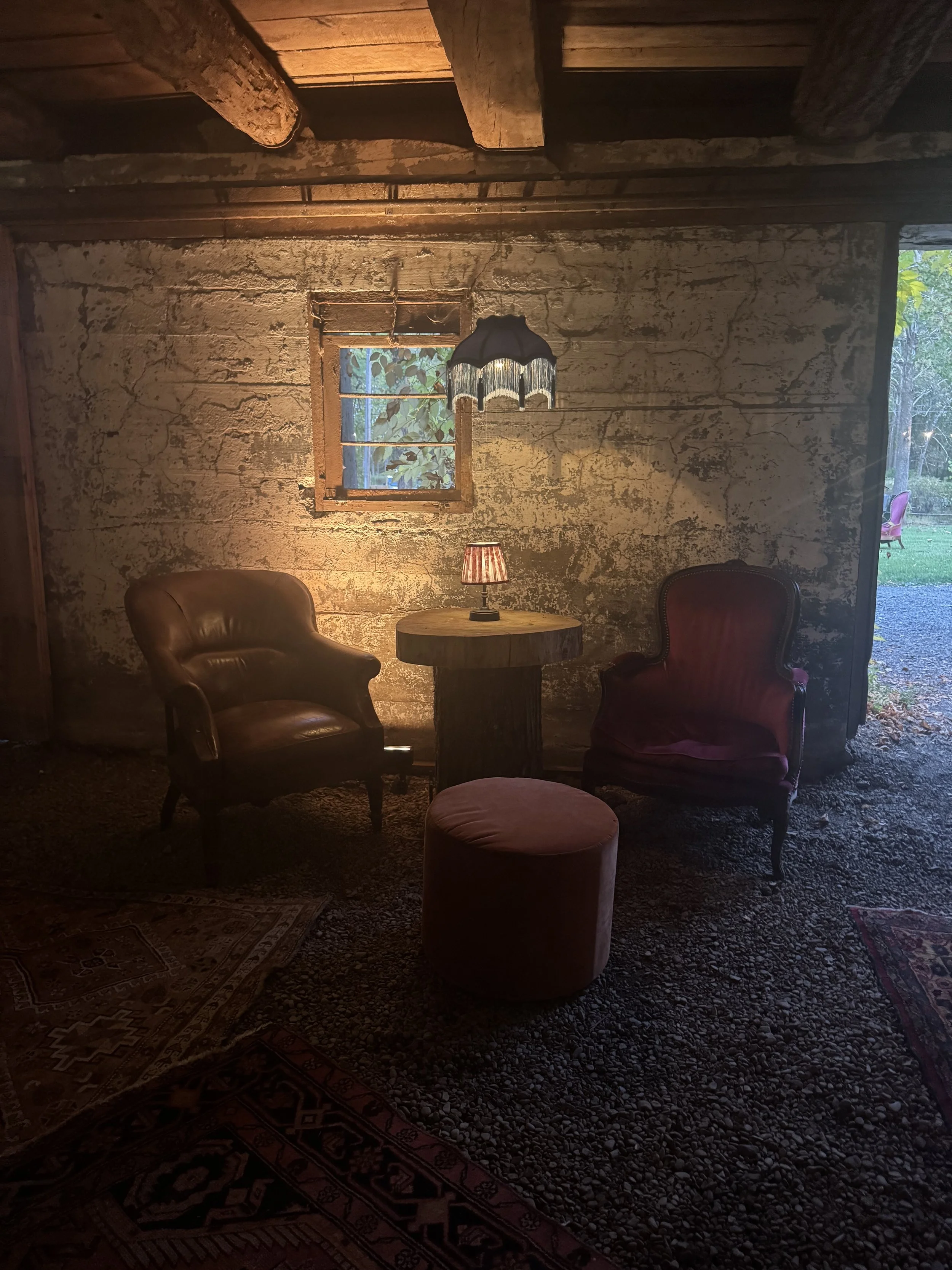 Rustic living room with leather sofa, striped chairs, wooden table, American flag on wall, wooden floors, and windows with outside greenery.