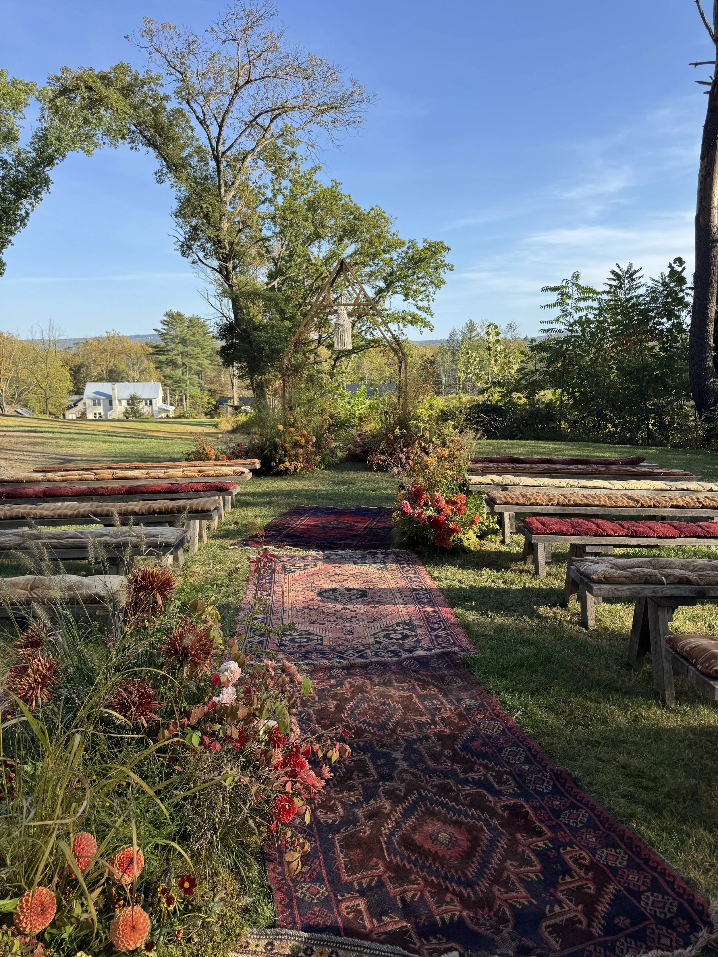 Outdoor wedding ceremony with two brides under a rustic chuppah, surrounded by greenery and floral arrangements in a forest setting.