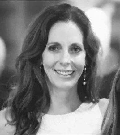 Smiling woman in black and white photo, wearing earrings and a light-colored top.