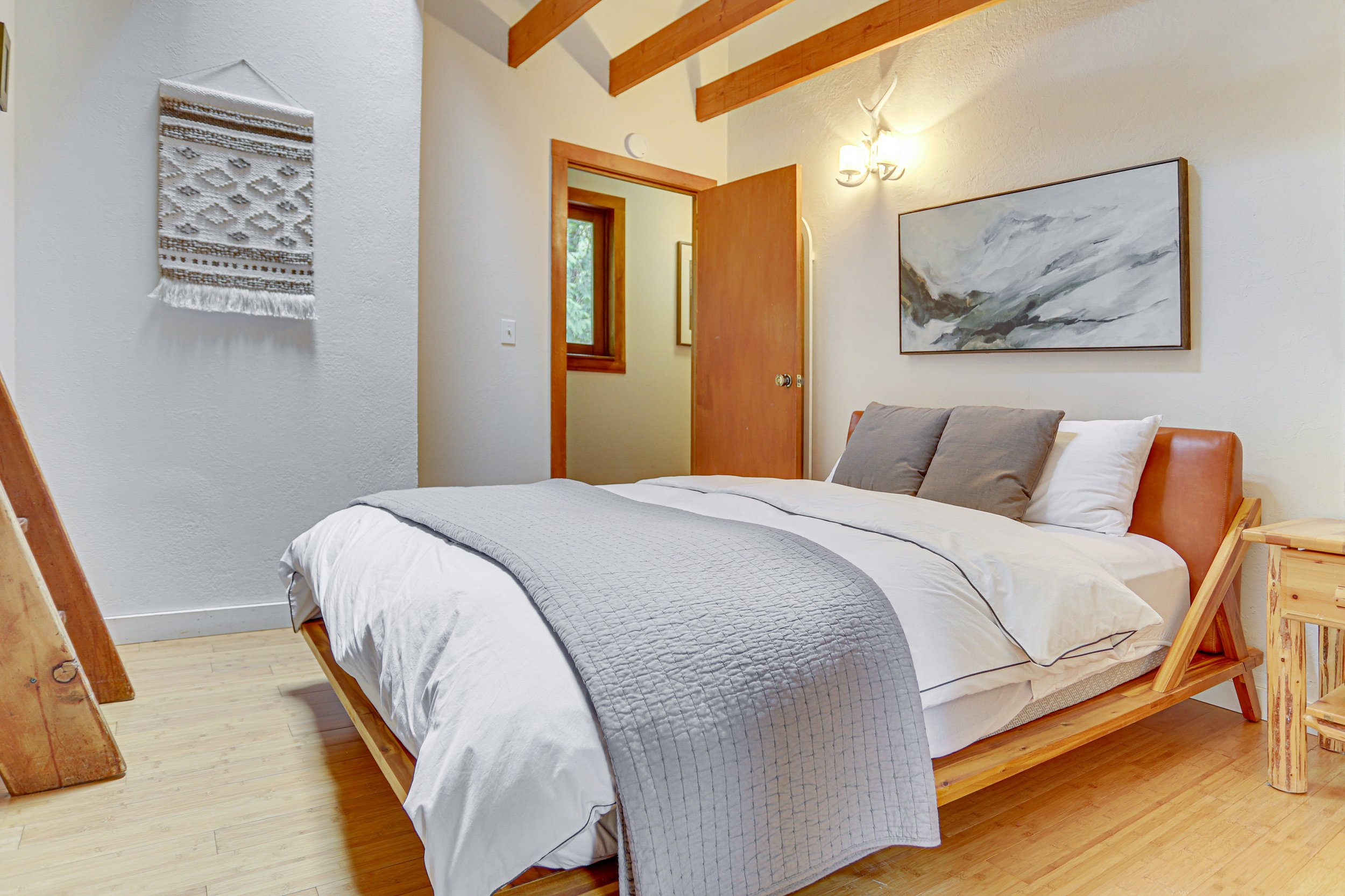 A second queen bedroom with a modern, leather headboard also looks up to a vaulted ceiling with exposed wood beams and a skylight.