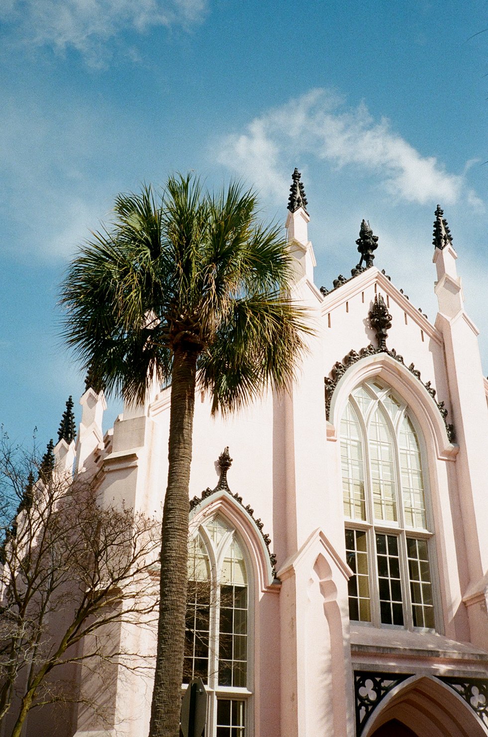 A Gothic-style pink church with tall arched windows and decorative spires, alongside a palm tree under a blue sky.