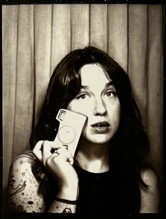 A four-panel photo booth picture of a woman with dark hair and tattoos, making different expressions and poses in front of a curtain background.