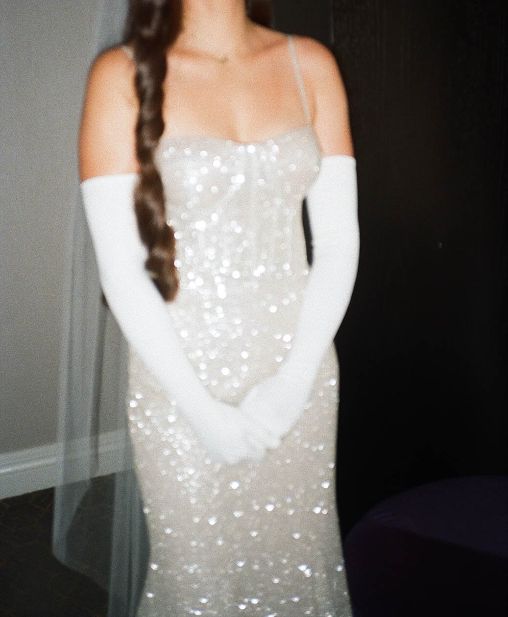 A woman in a sparkly sequin dress with white gloves and a long braid. The image is slightly blurry.