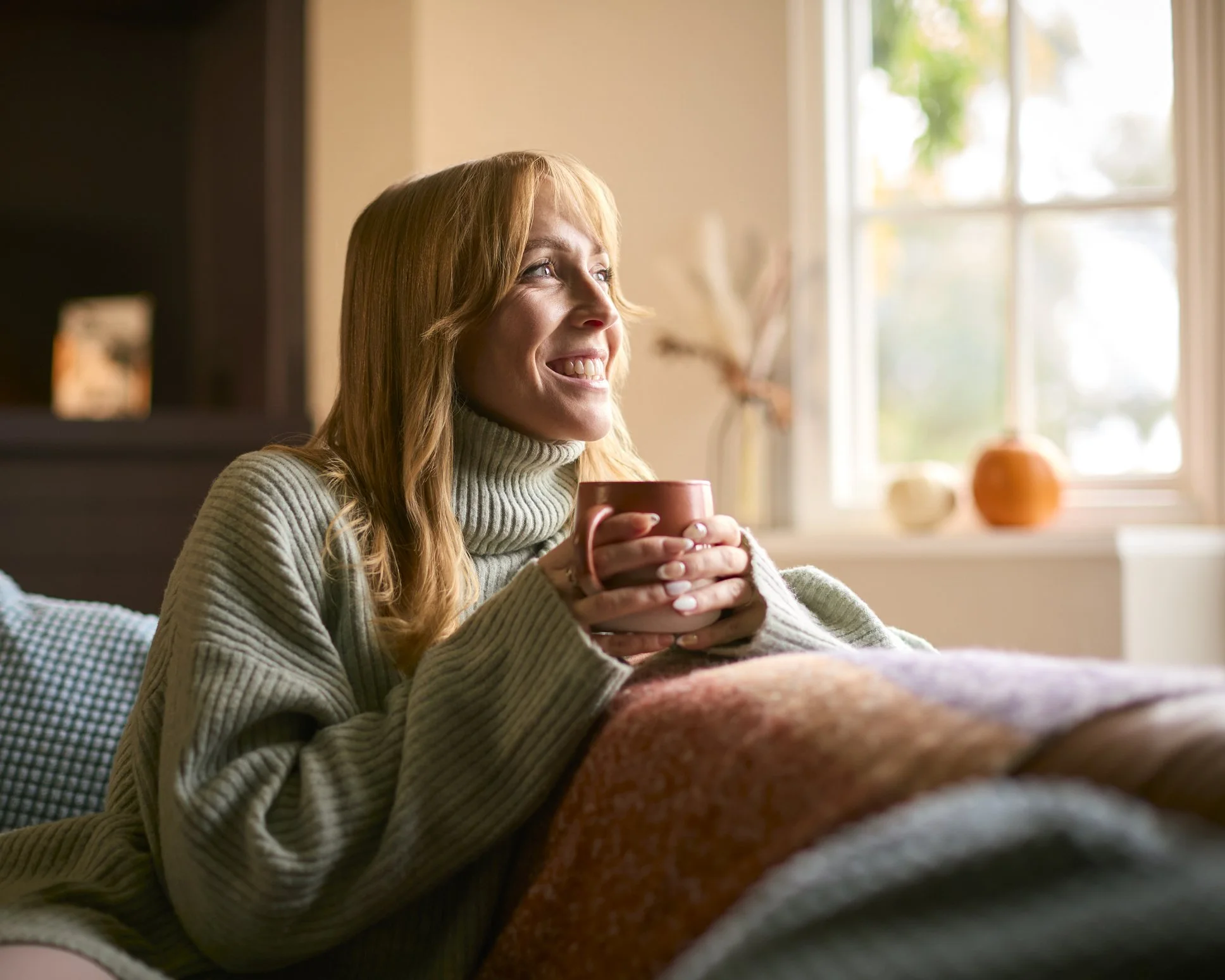 Woman holding mug and smiling on couch during therapy for panic attacks in Reston, VA