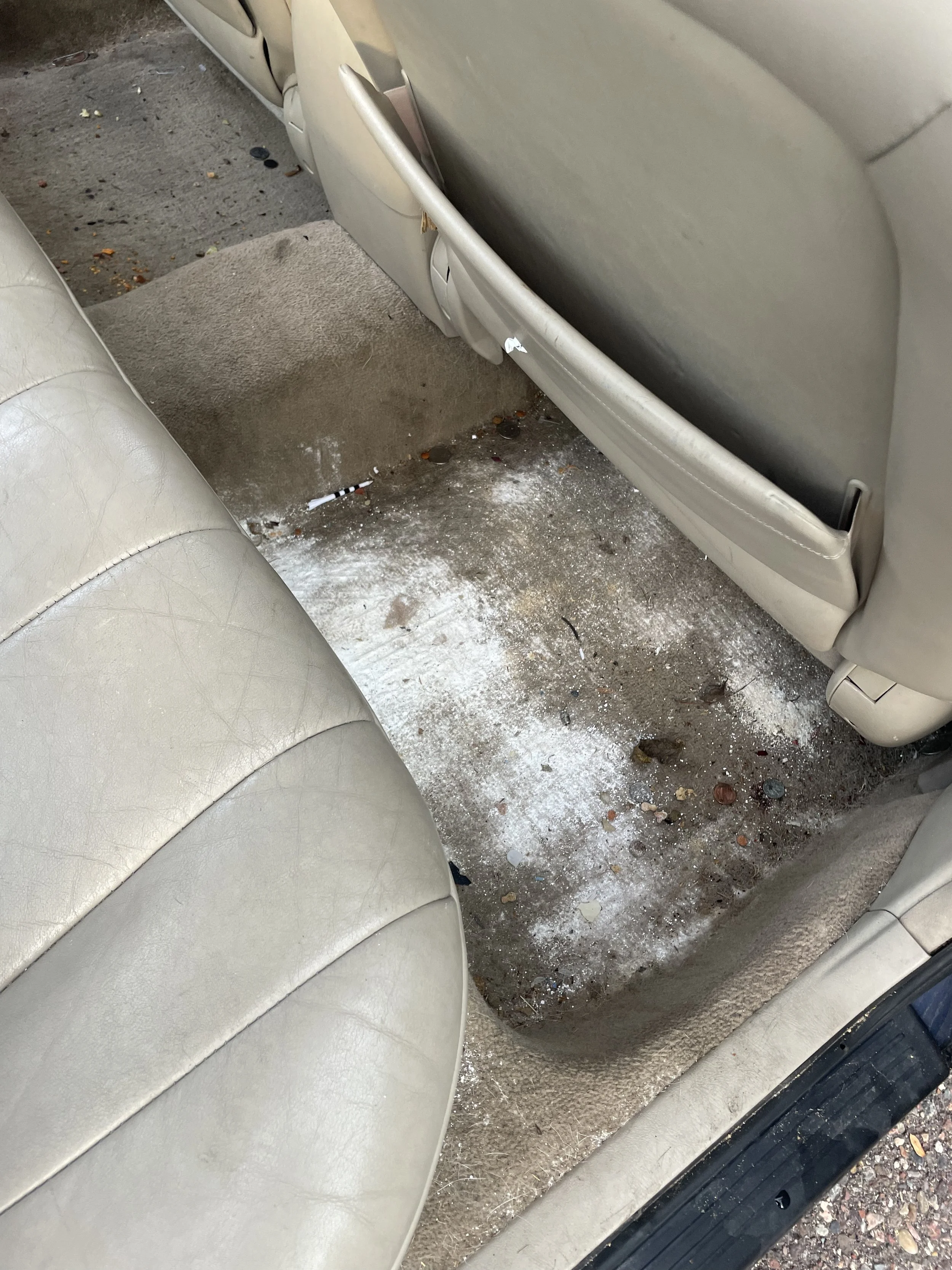 Dirty car floor with spilled powder, cigarette butts, and debris inside a beige car.