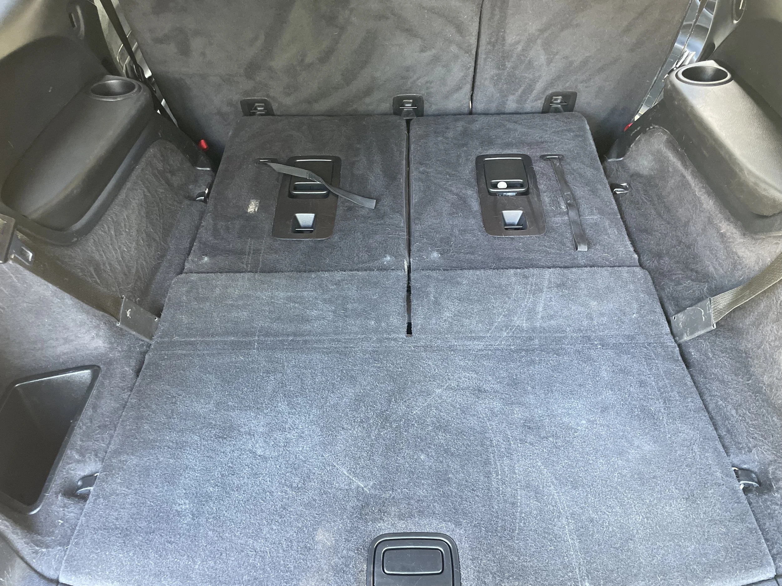 Interior of a vehicle with folded-down rear seats, revealing an expanded cargo space with black fabric upholstery and seat lock mechanisms.