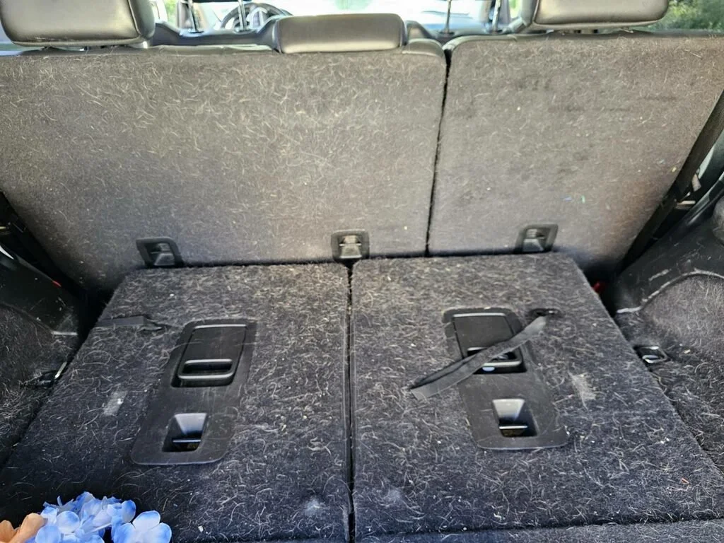 Back seats of a car with the seats folded down, showing dirt, hair, and some debris on the fabric.