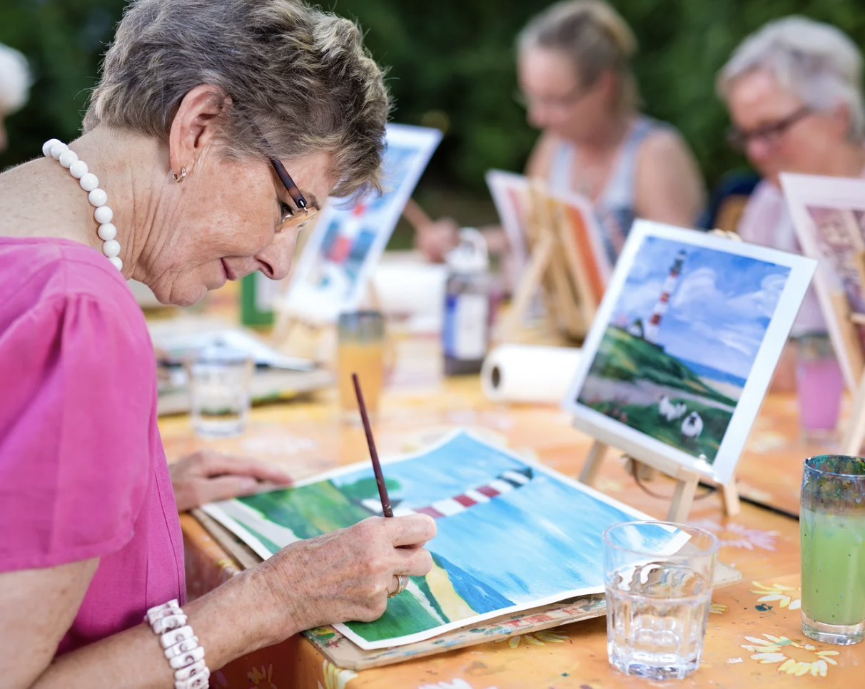 Woman painting at a table during a therapeutic activity, representing focus and skill-building in CBT therapy.