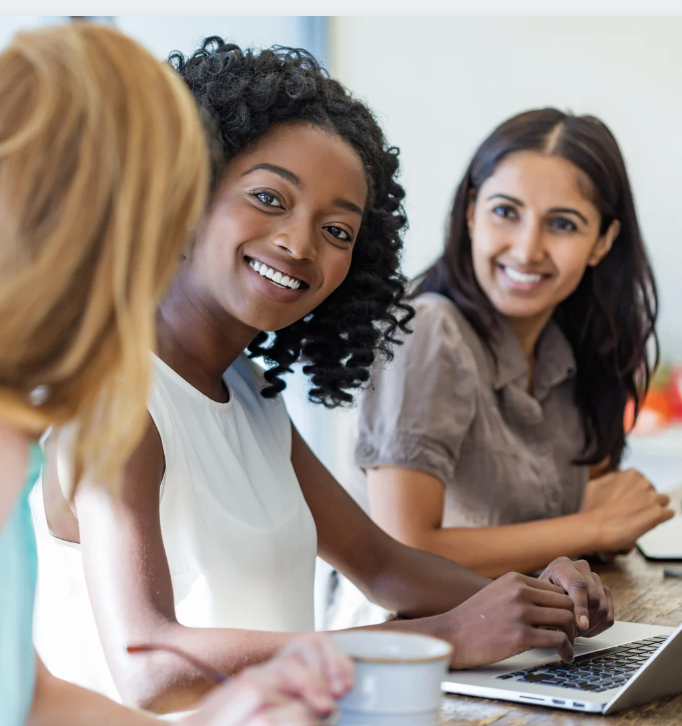 Three women sitting together at a table with a laptop during hello DBT therapy.