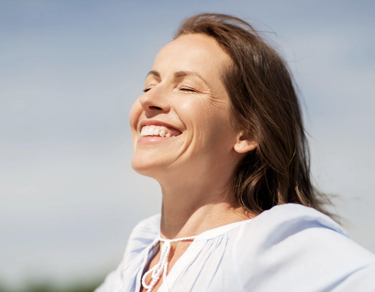 Woman smiling with eyes closed outdoors, representing calm and emotional relief with hello CBT therapy.