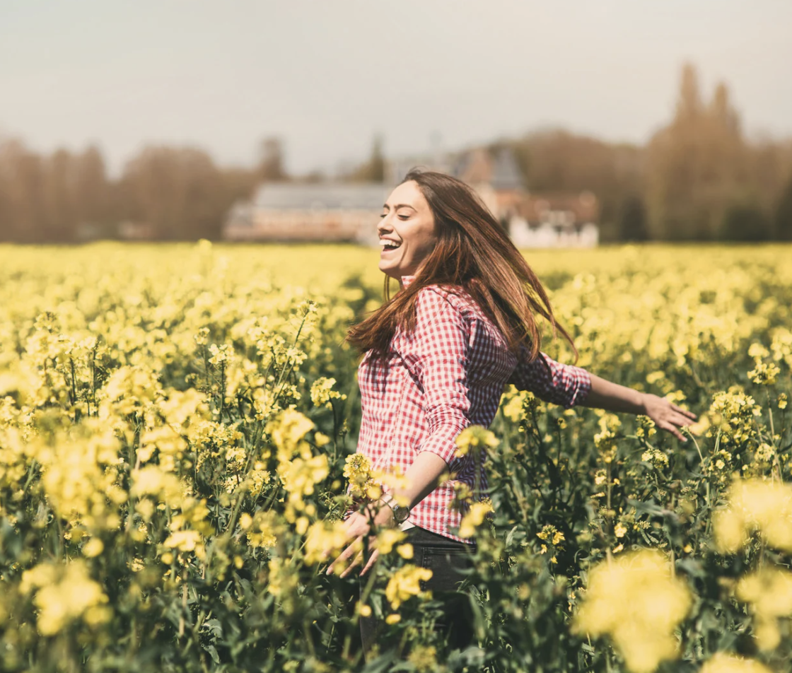 Woman walking through a field of yellow flowers outdoors, associated with hello CBT therapy.