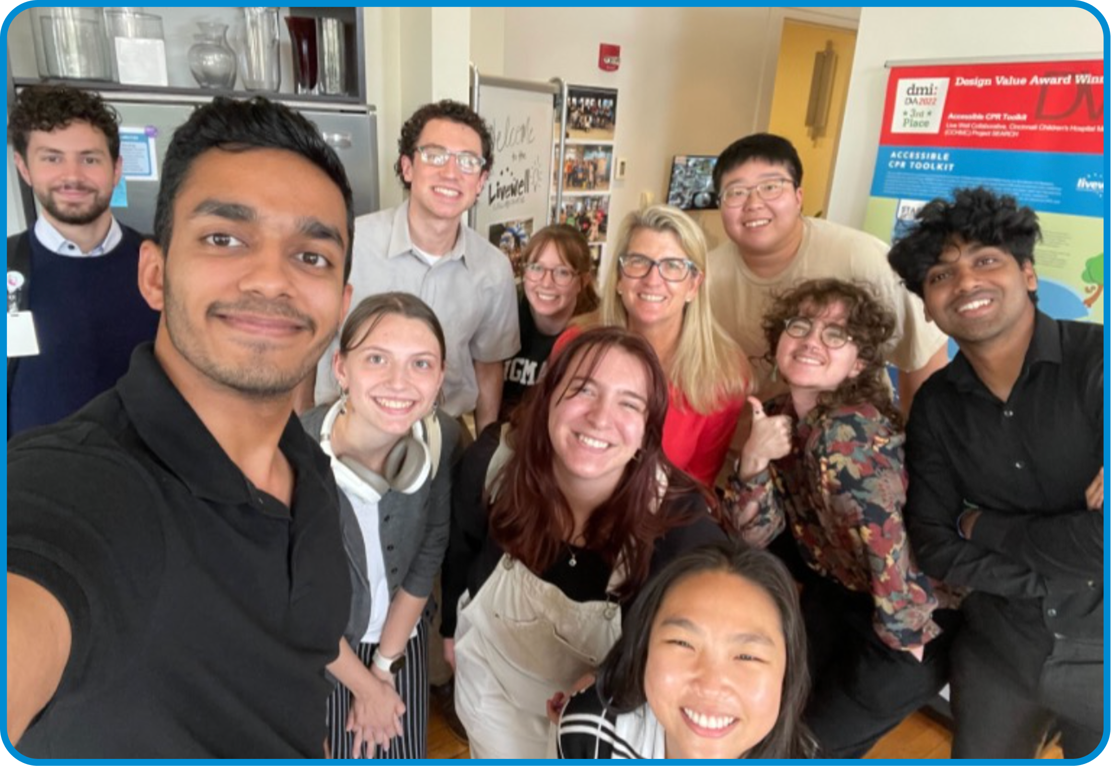 Group of smiling people taking a selfie in an indoor setting with posters on the wall.
