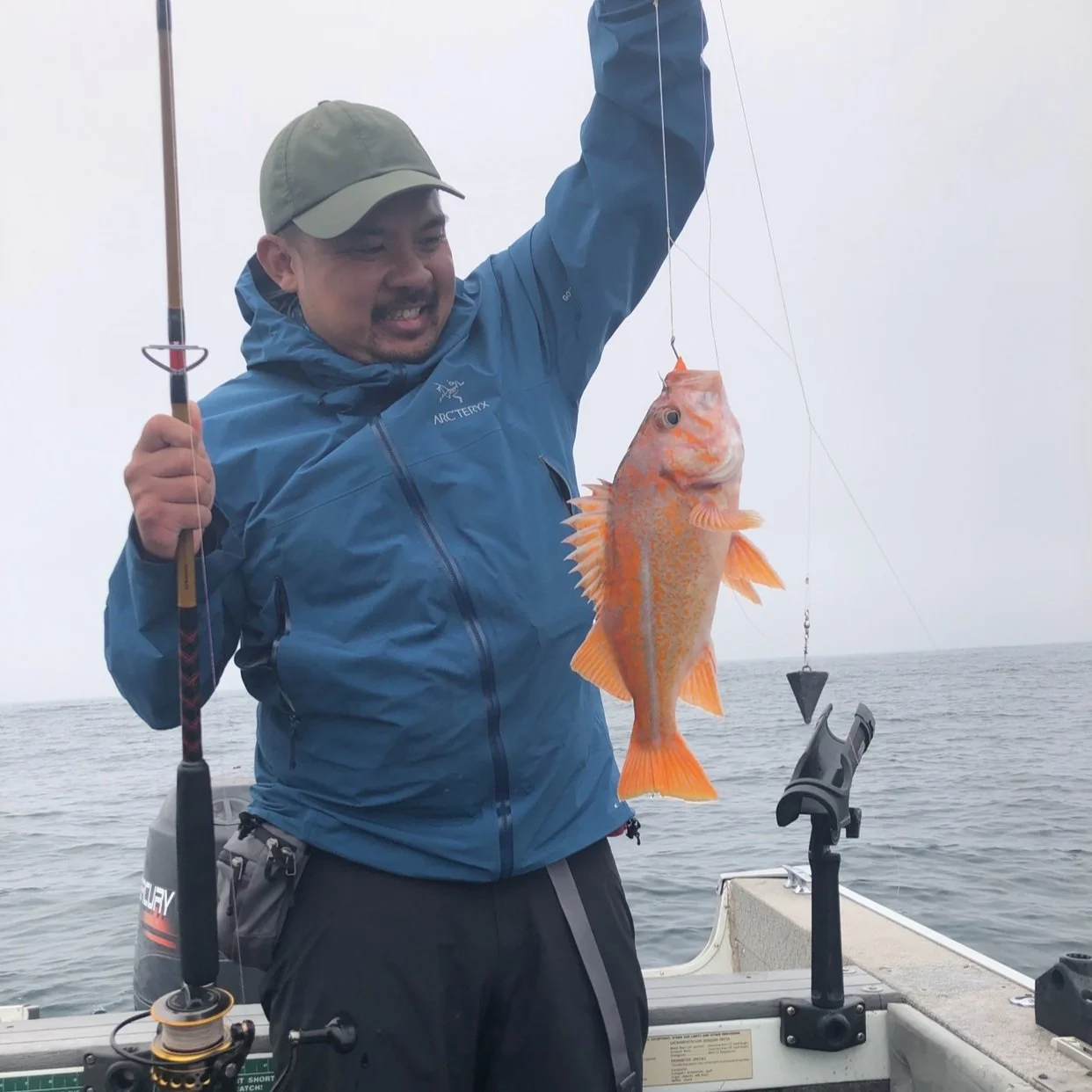 Trac Hoang pictured on a boat. He is holding his catch, a golden colored snapper, and has a fishing pole in the other hand. He is smiling widely down at the fish.