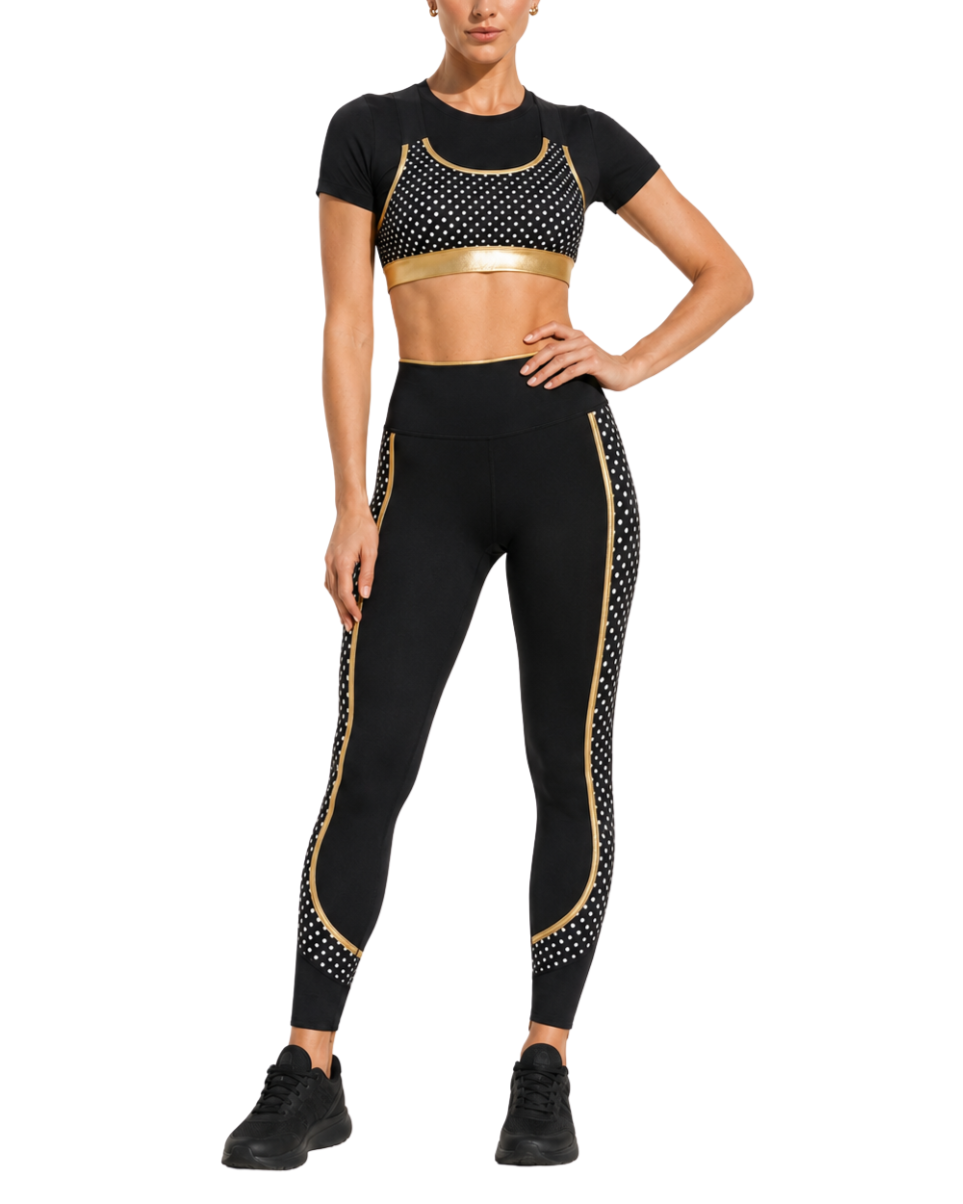 A woman wearing a sporty black outfit with gold accents and white polka dots, standing with one hand on her hip.