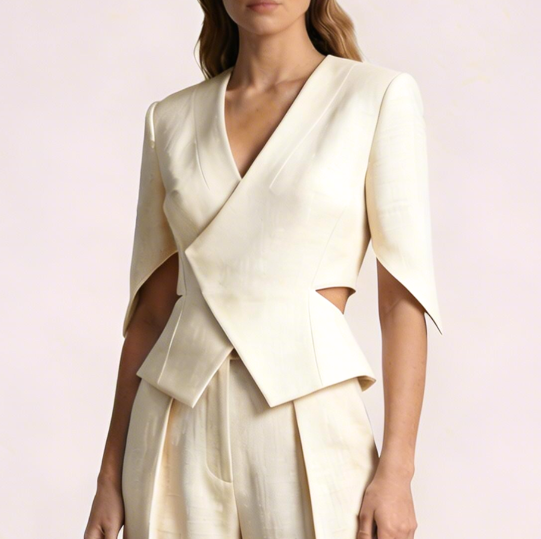 Woman wearing an elegant off-white tailored blazer with matching high-waisted pants, standing against a light background.