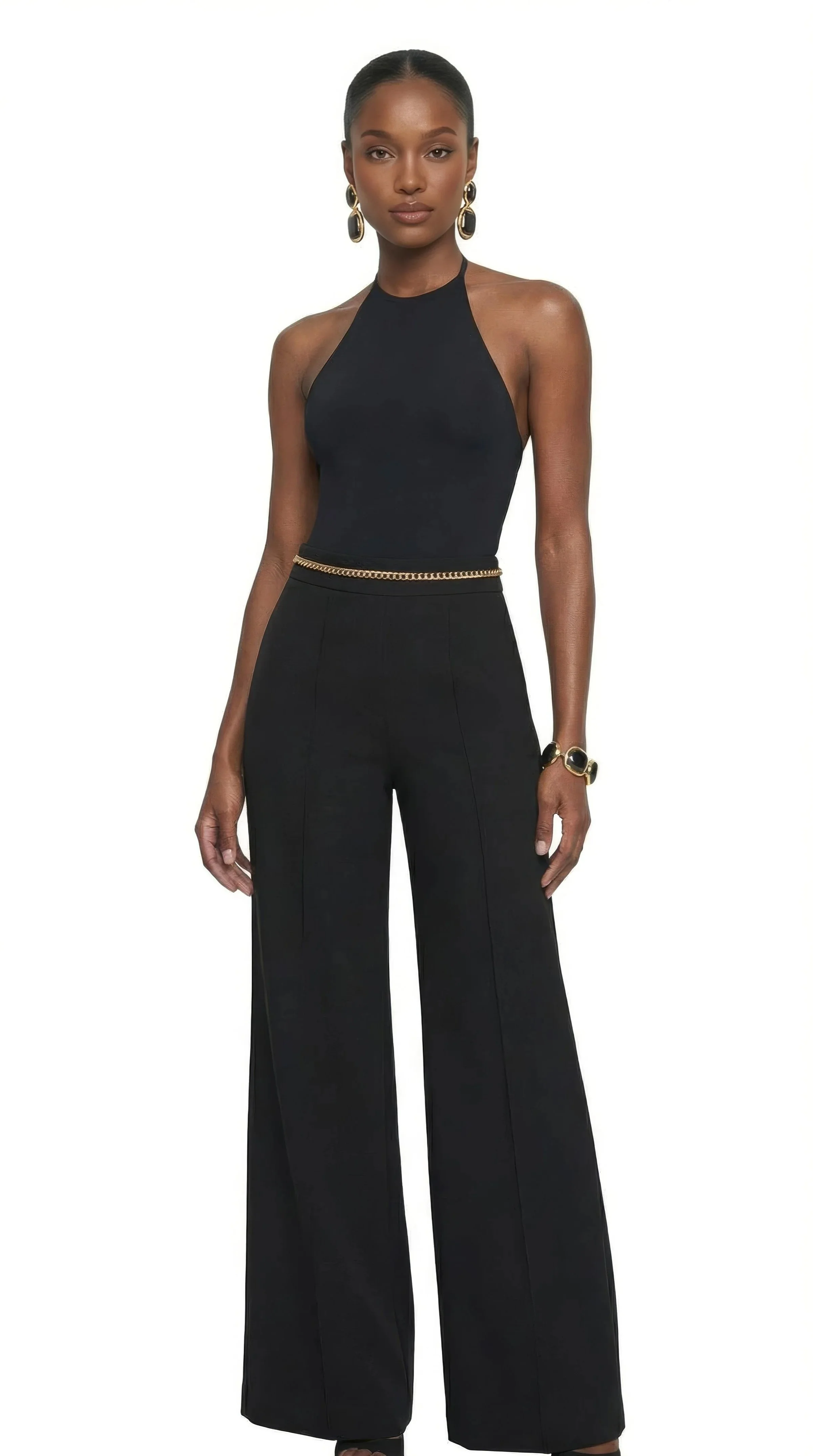 A woman with dark skin and a sleek hairstyle, dressed in a black halter top and matching high-waisted wide-leg pants, accessorized with gold earrings, a chain belt, and a bracelet, posing against a white background.