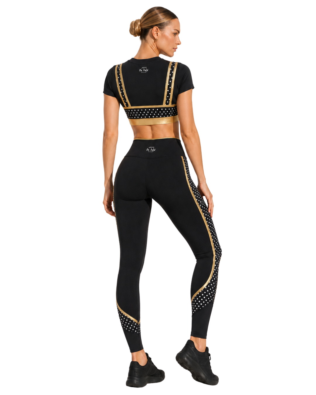 Woman in black athletic wear with gold and white polka dot accents, standing with her back to the camera, showcasing a sporty outdoor outfit.