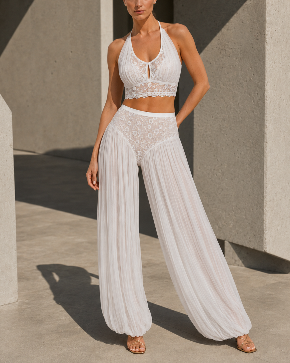 A woman wearing a white lace and pleated wide-leg pants outfit standing outdoors in sunlight.