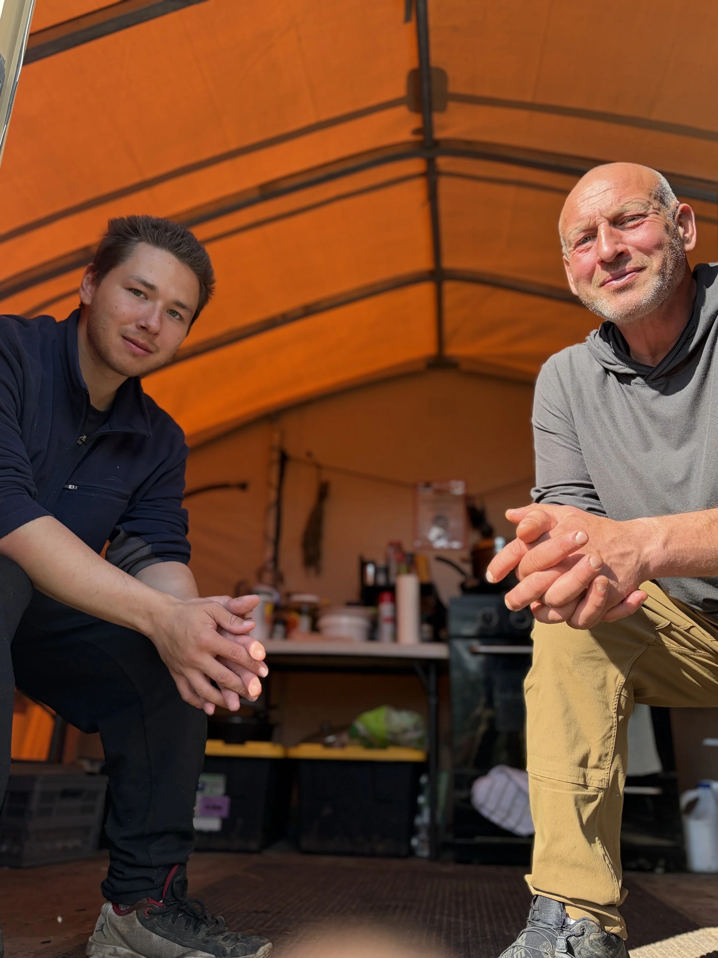 cooking in a small outdoor kitchen tent, with a stove, kettle, and spices visible.